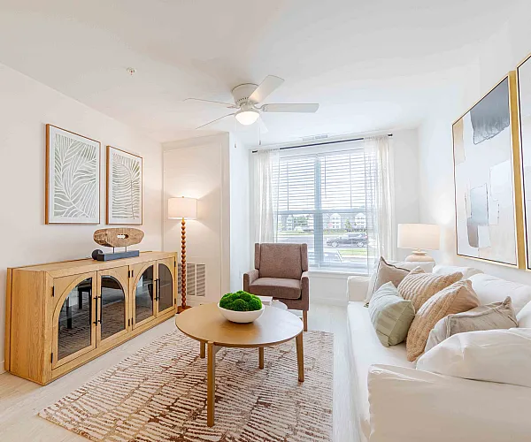 Bright and inviting living room with large window, modern decor, and stylish furnishings. Cozy glimpses of a serene bedroom add to the peaceful ambiance.