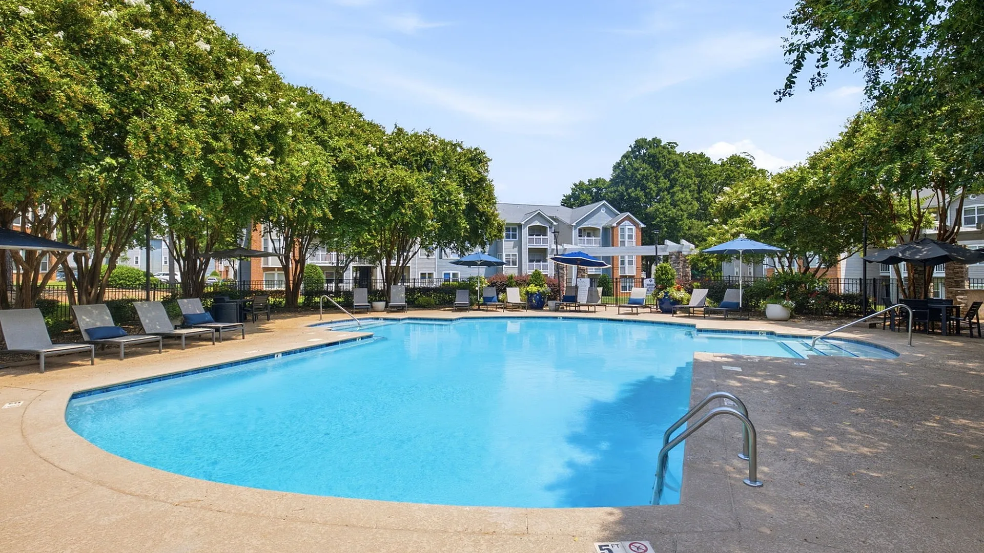 Inviting outdoor pool area with sun loungers and umbrellas surrounded by lush greenery, perfect for relaxation and leisure.
