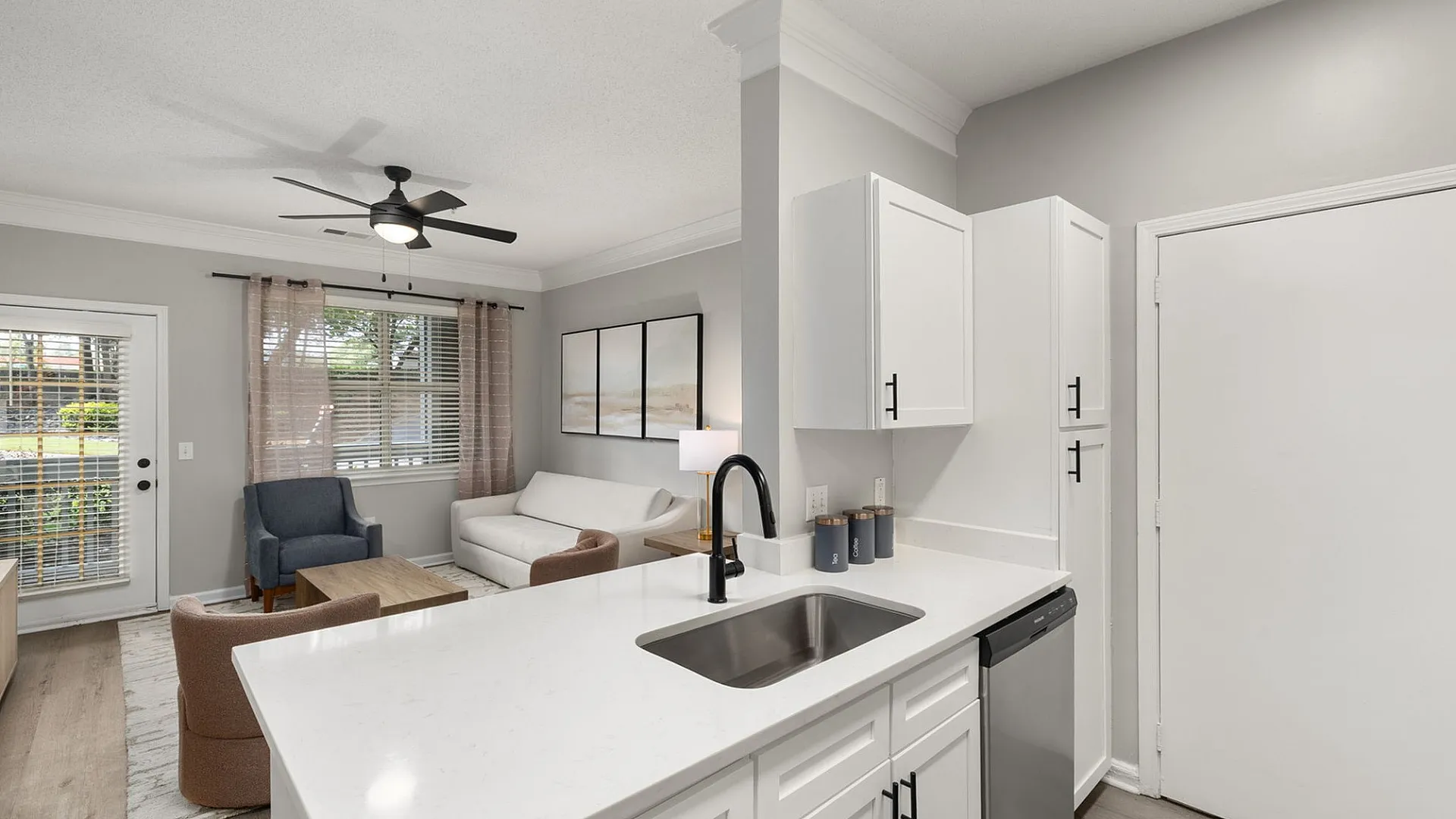 Modern open-concept living room and kitchen with sleek white cabinetry, cozy seating area, and abundant natural light.