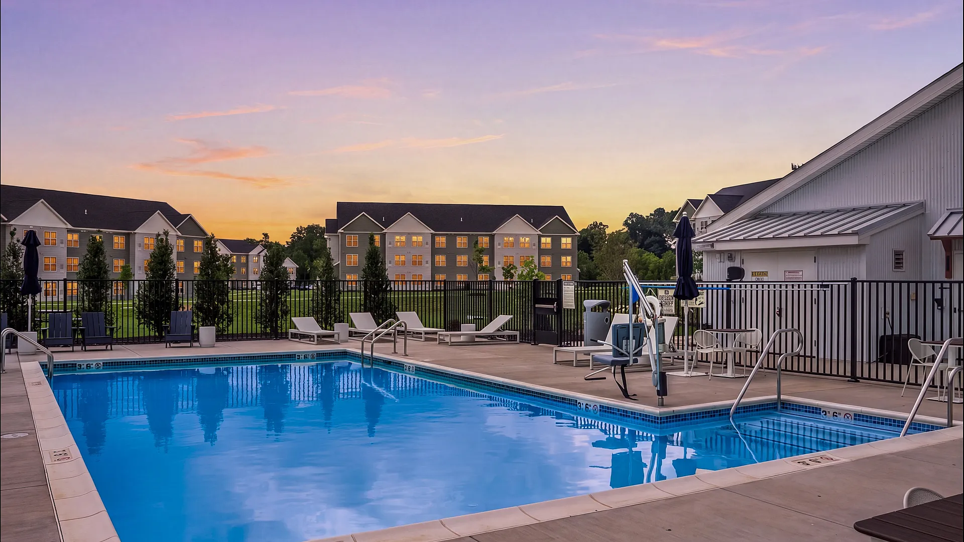 Inviting outdoor pool area with stylish lounge chairs, set against a serene sunset backdrop and modern apartment buildings.