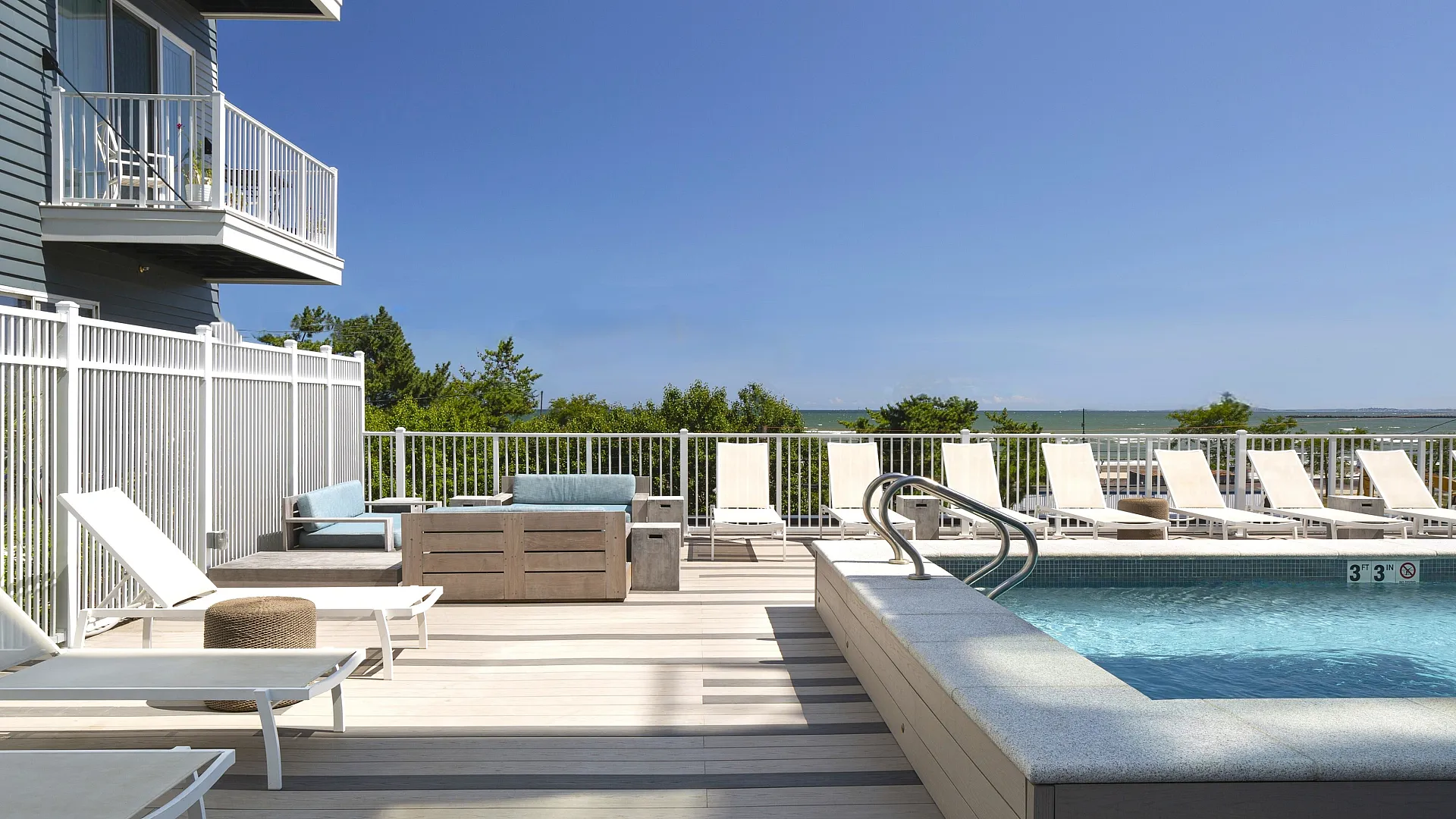 Luxurious balcony pool deck with sleek lounge chairs, coastal views, and upscale modern seating.