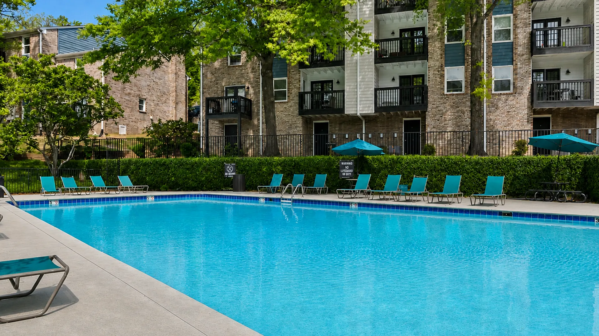 Inviting apartment complex with a sparkling outdoor pool surrounded by lush greenery and modern balconies.