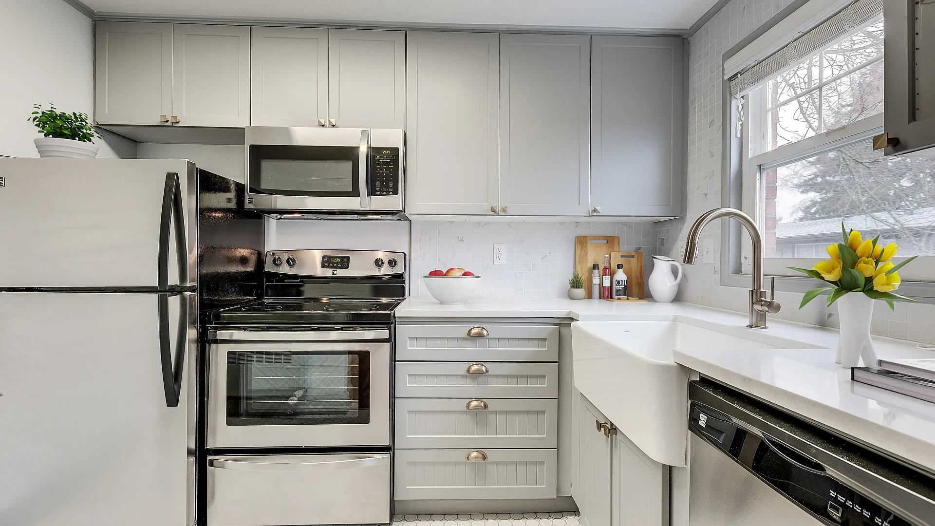 Modern kitchen with sleek stainless steel appliances, chic grey cabinetry, and bright natural light from a large window adorned with fresh flowers.