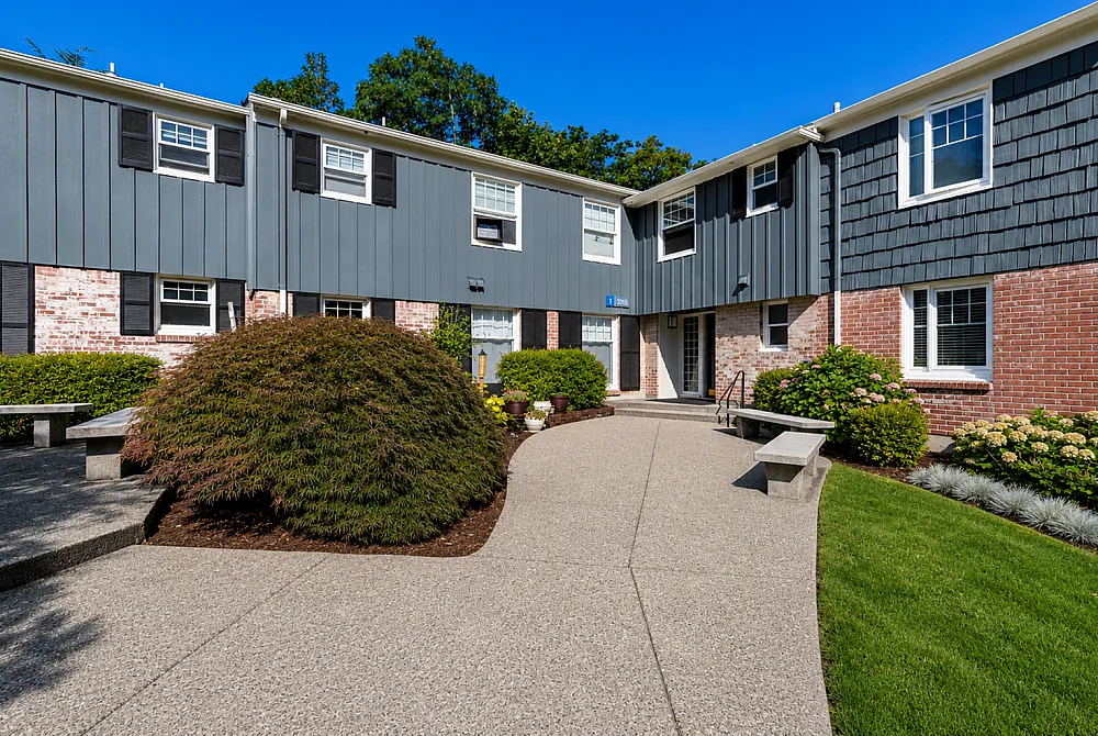 Charming apartment complex exterior with manicured shrubs, brick and siding facade, nestled in lush greenery.