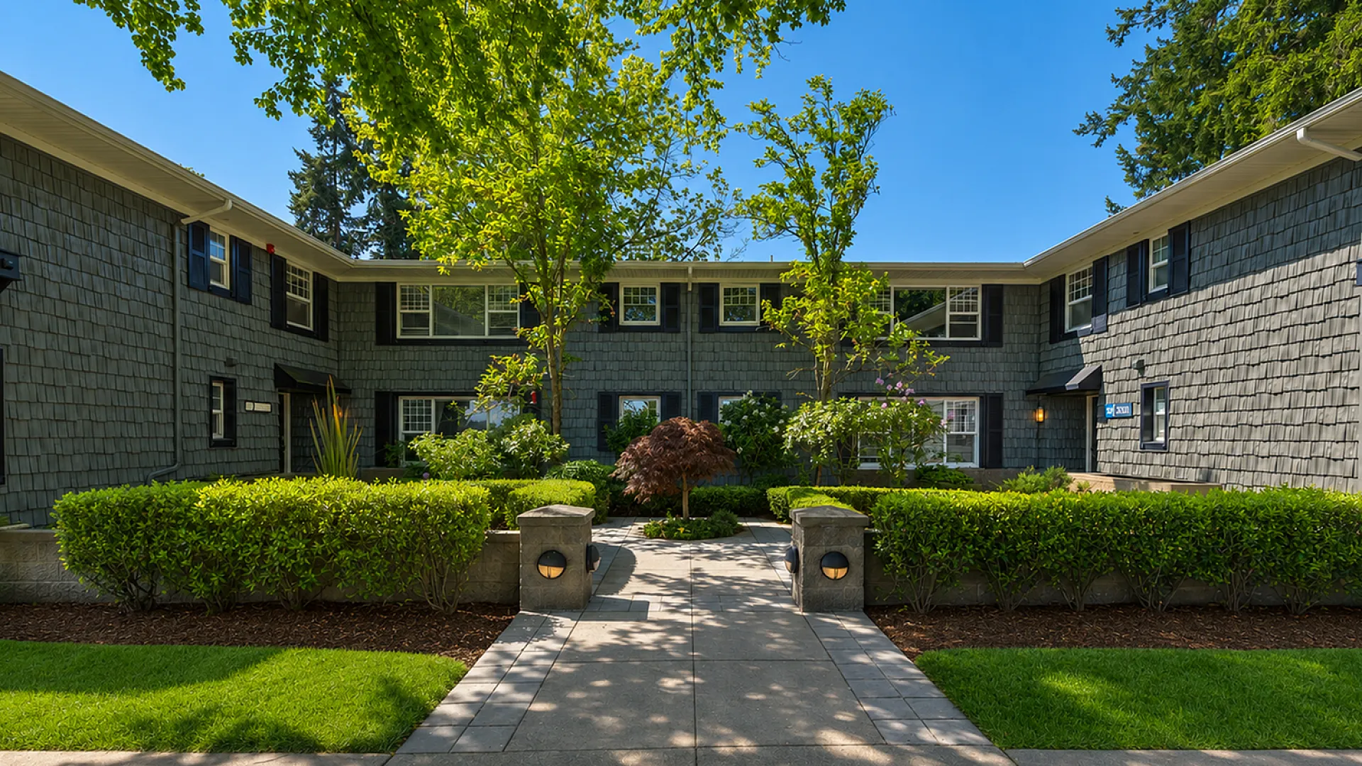 Charming two-story apartment building with lush landscaped gardens and mature trees, creating a serene, welcoming atmosphere.