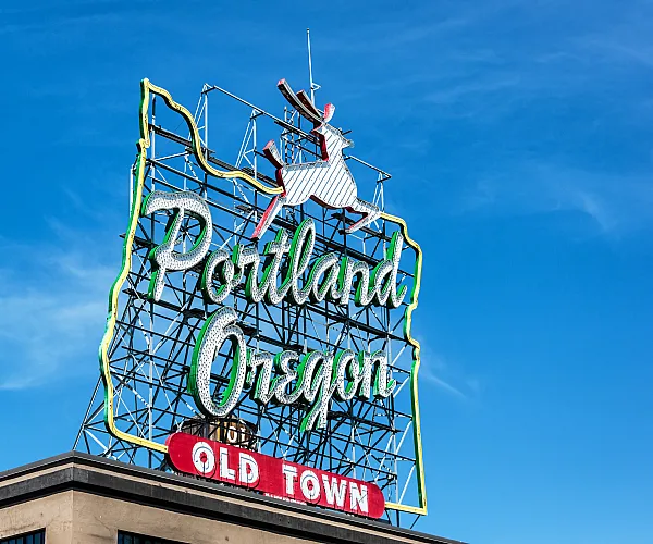 Iconic Portland Oregon neon sign against a vibrant blue sky, adding charm to the historic Old Town district.