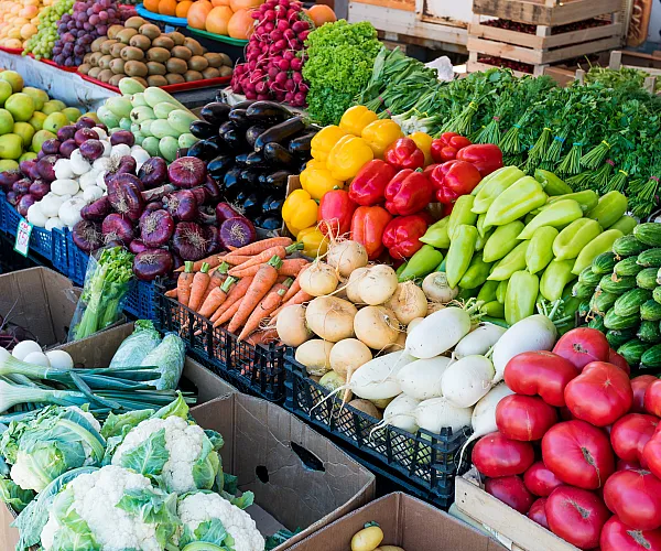 Vibrant market stall showcasing a colorful array of fresh vegetables including bell peppers, radishes, carrots, and eggplants.