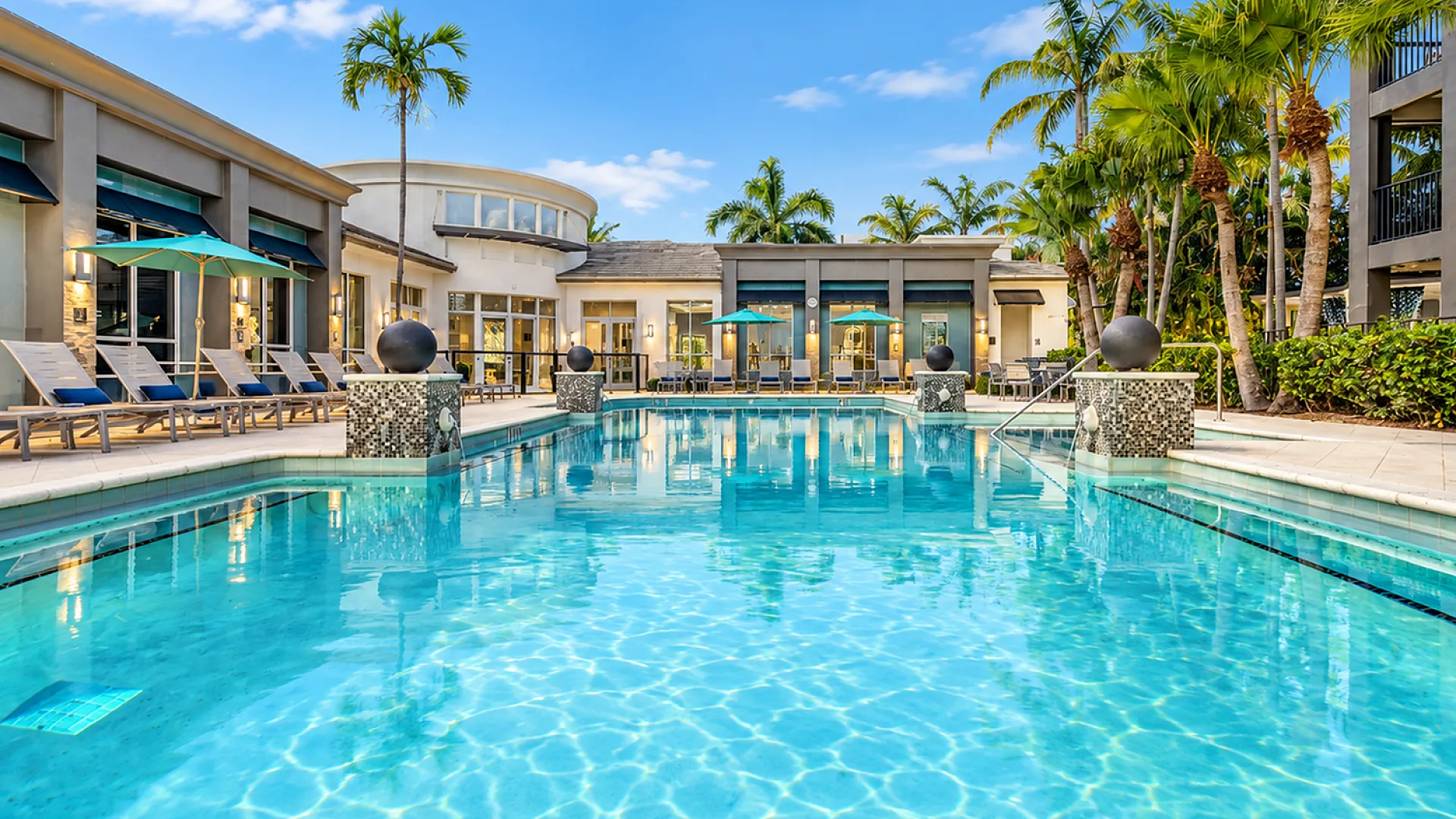 Luxurious apartment complex with a sparkling pool, surrounded by palm trees and modern architecture, offering a resort-style living experience.