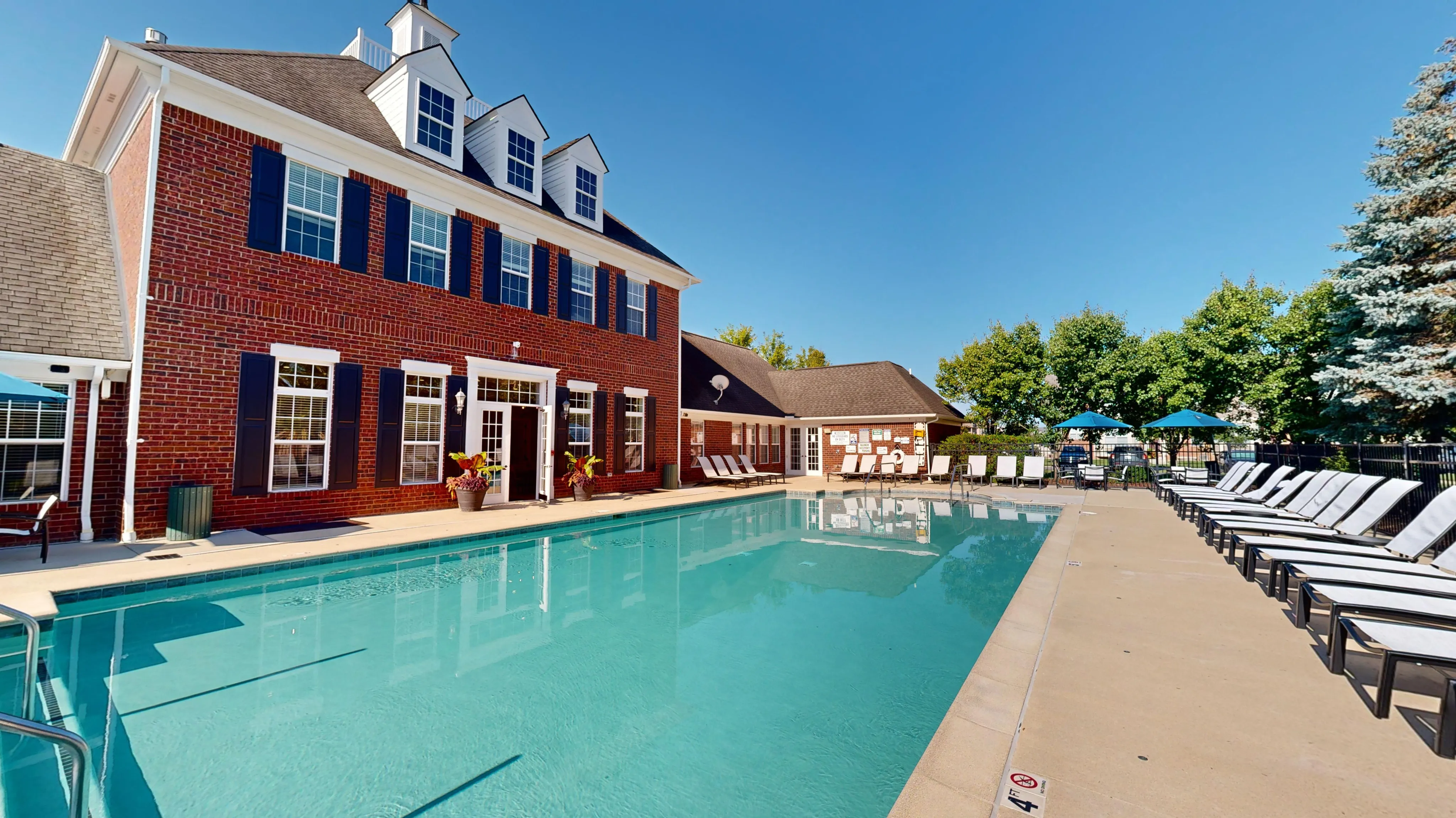 Elegant brick apartment complex with a refreshing outdoor swimming pool and ample sun loungers, perfect for relaxation and leisure.
