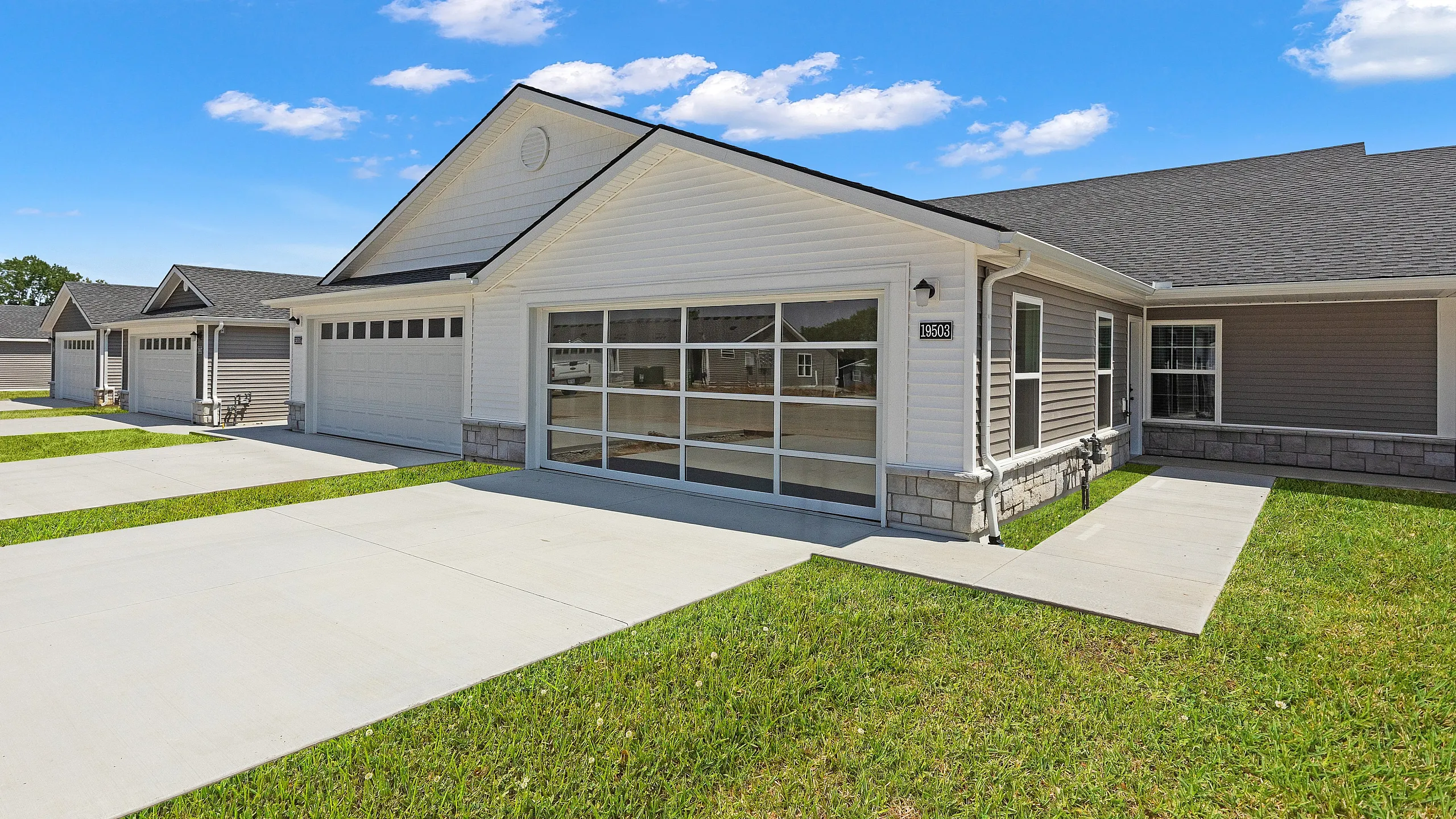 Modern single-story townhouse with a sleek white facade, spacious driveway, and manicured lawn on a sunny day.