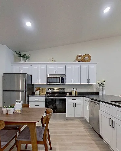 Modern kitchen and dining area featuring sleek white cabinetry, a polished granite countertop, and stainless steel appliances, complemented by a cozy wooden dining table for a warm, inviting space.