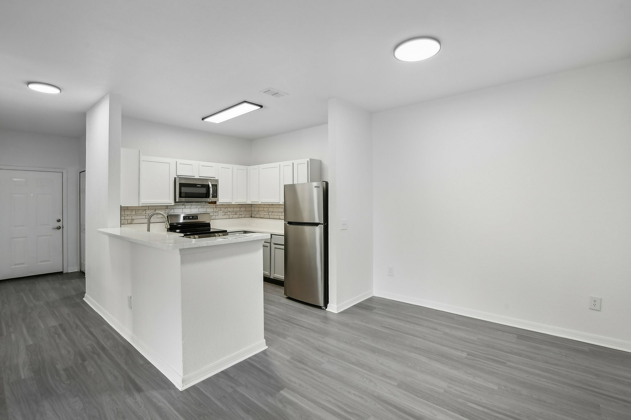 interior pic of deluxe unit kitchen with gray planking and white walls, stainless steel appliances, white cabinets and tile backsplash