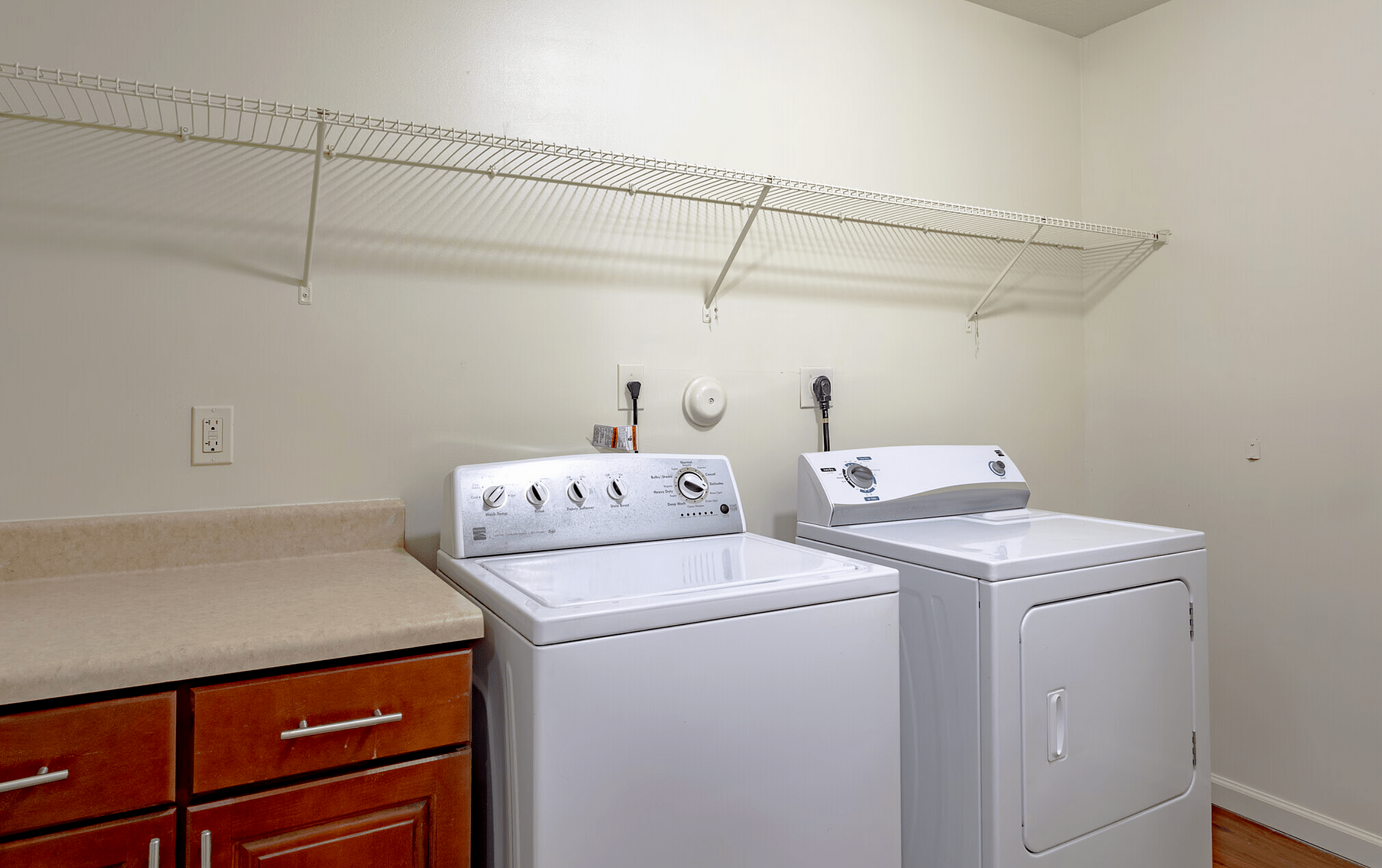 In-unit laundry room with washer and dryer, countertop, cabinet storage, and overhead wire shelving.