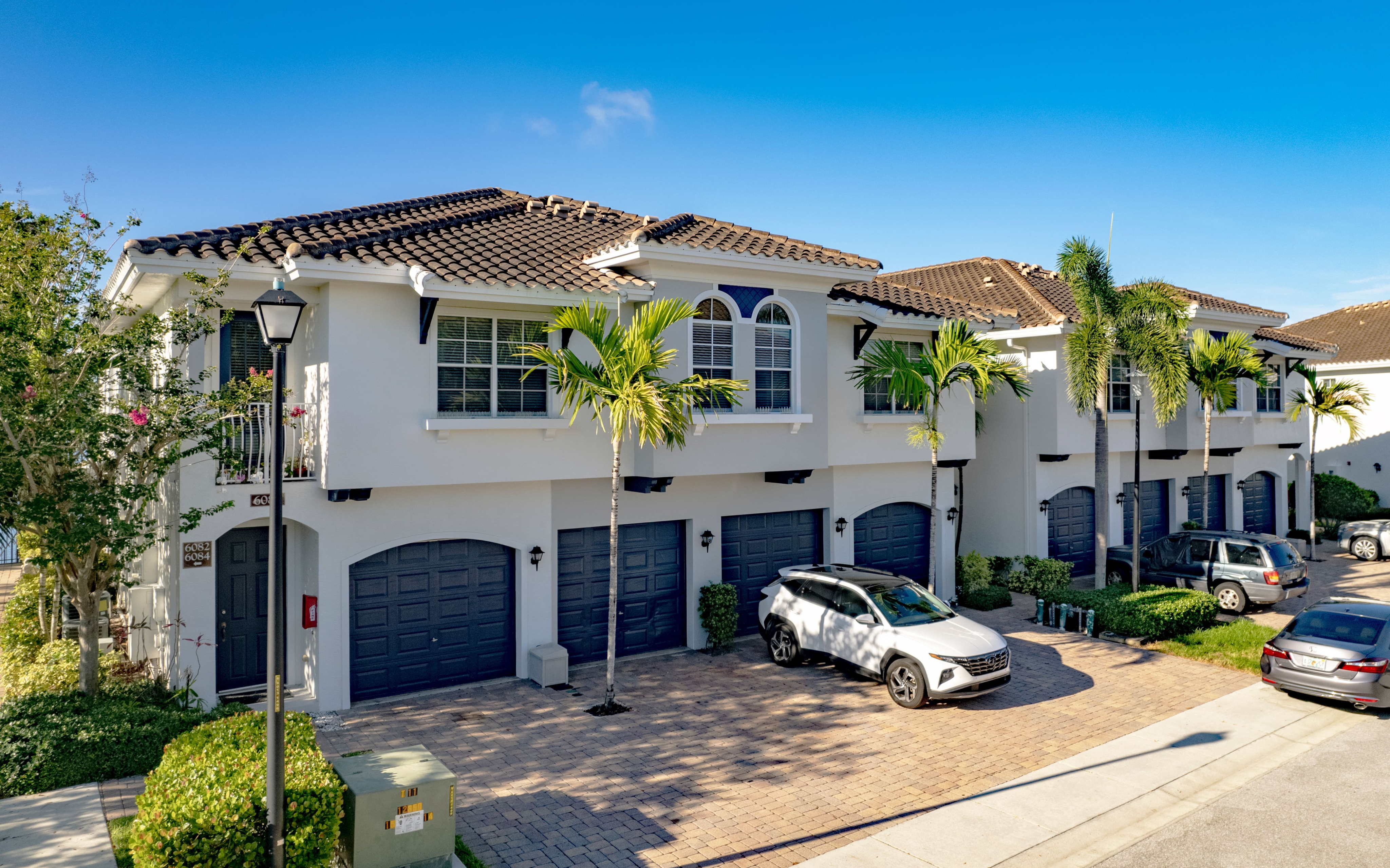 Charming Mediterranean-style townhomes with tile roofs, palm trees, and attached garages under a bright blue sky.