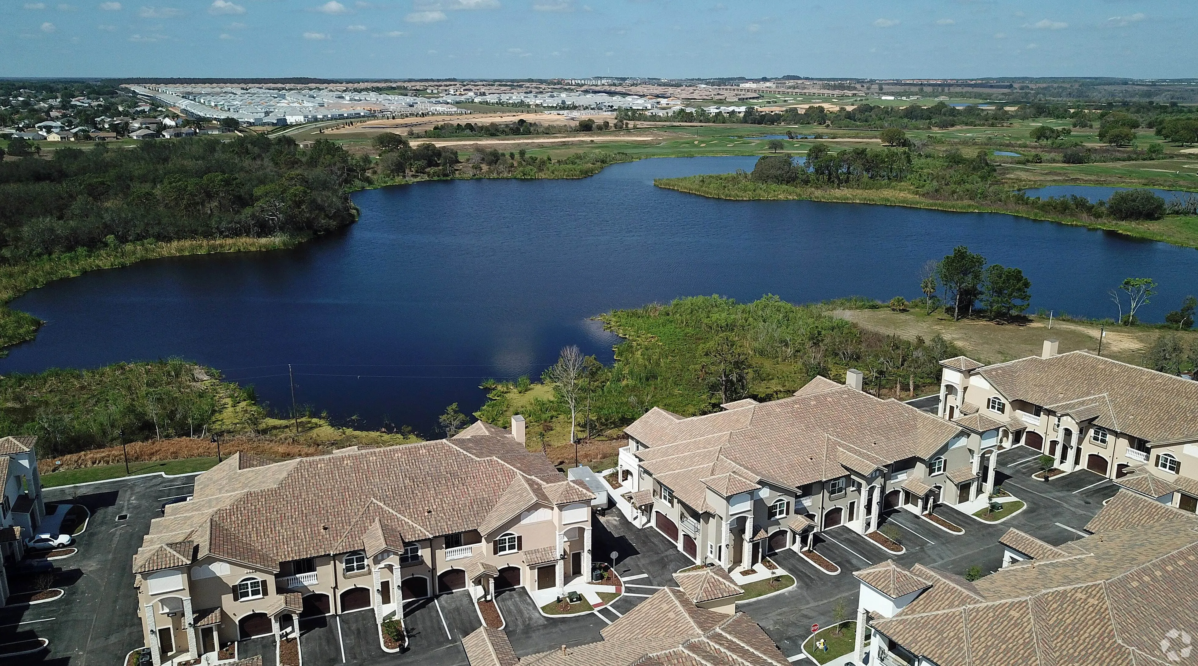 Breathtaking aerial view of a modern lakeside apartment complex surrounded by lush greenery and expansive scenic water views.