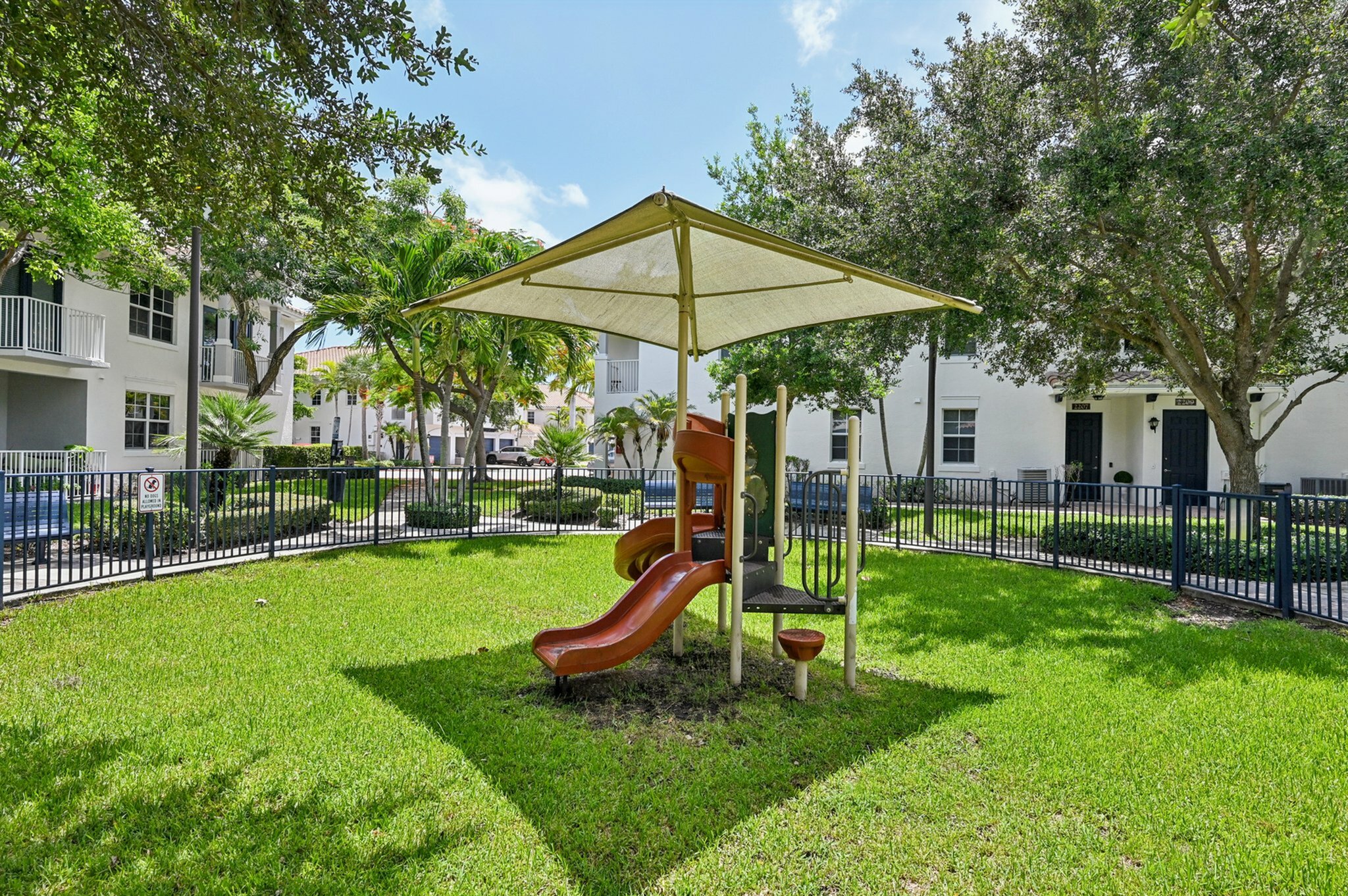 Vibrant playground with slide, surrounded by lush greenery and shade structures.