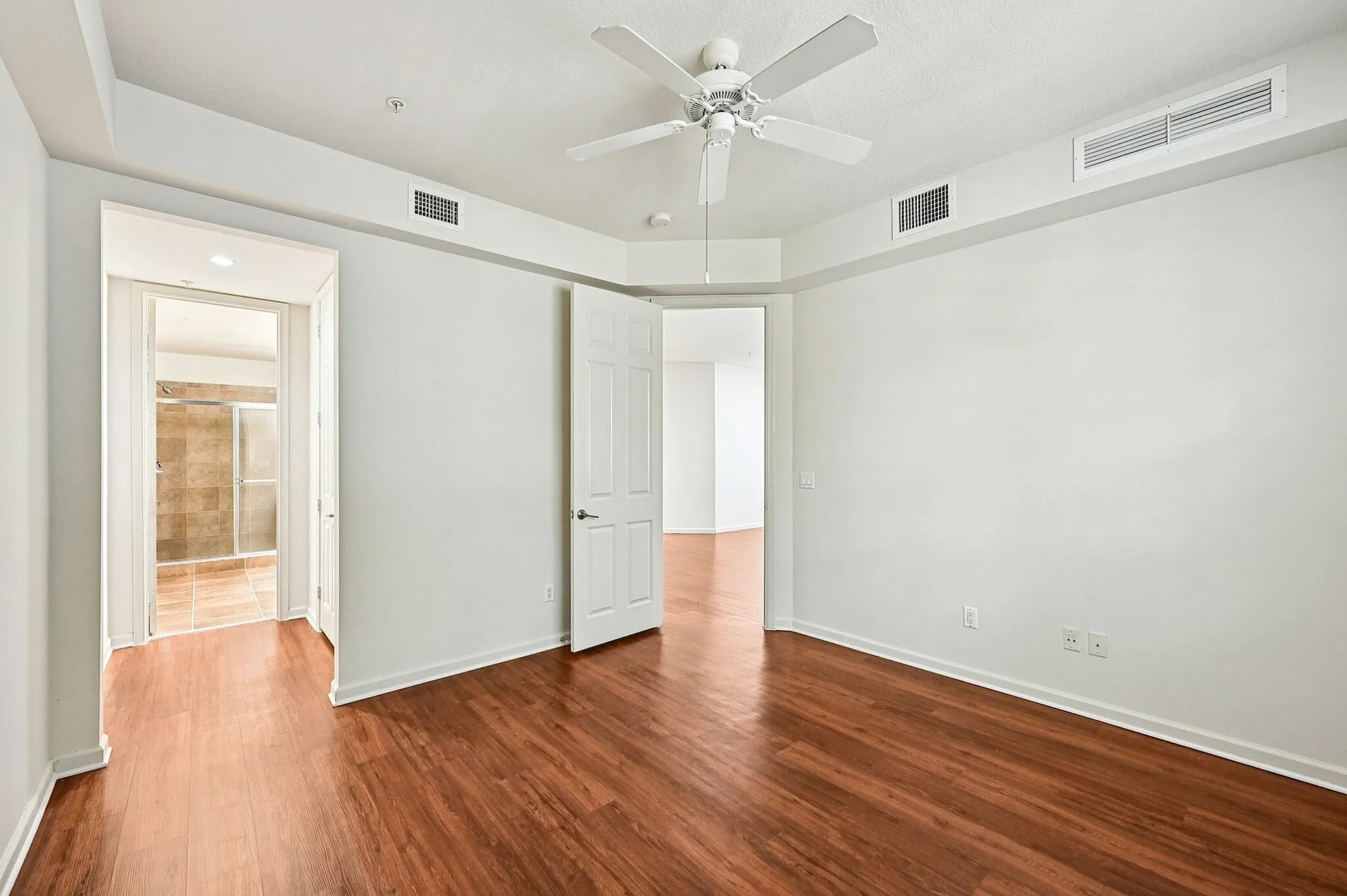 Modern apartment room with wooden flooring, a ceiling fan, and an en-suite bathroom featuring elegant tile work.