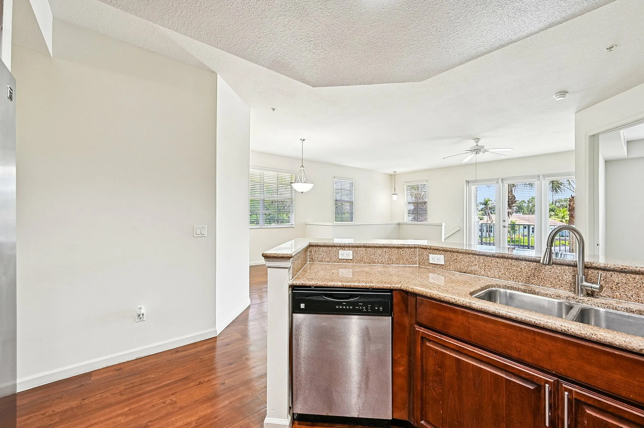 Bright, open-concept living area showcasing sleek granite countertops, stainless steel appliances, and a warm, inviting wooden floor.