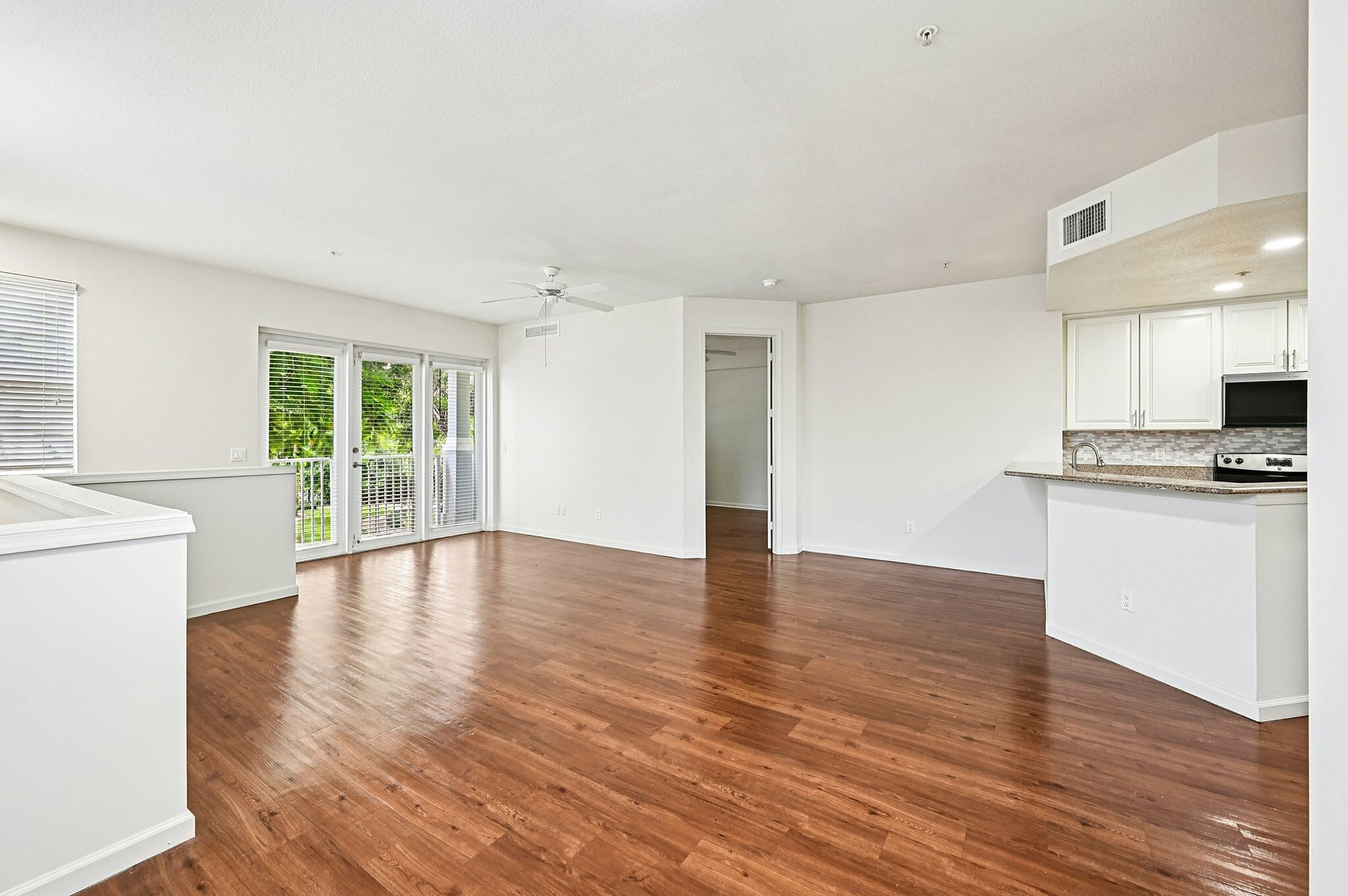 Bright and spacious apartment with elegant wooden flooring, open-concept kitchen, and expansive windows overlooking lush greenery.