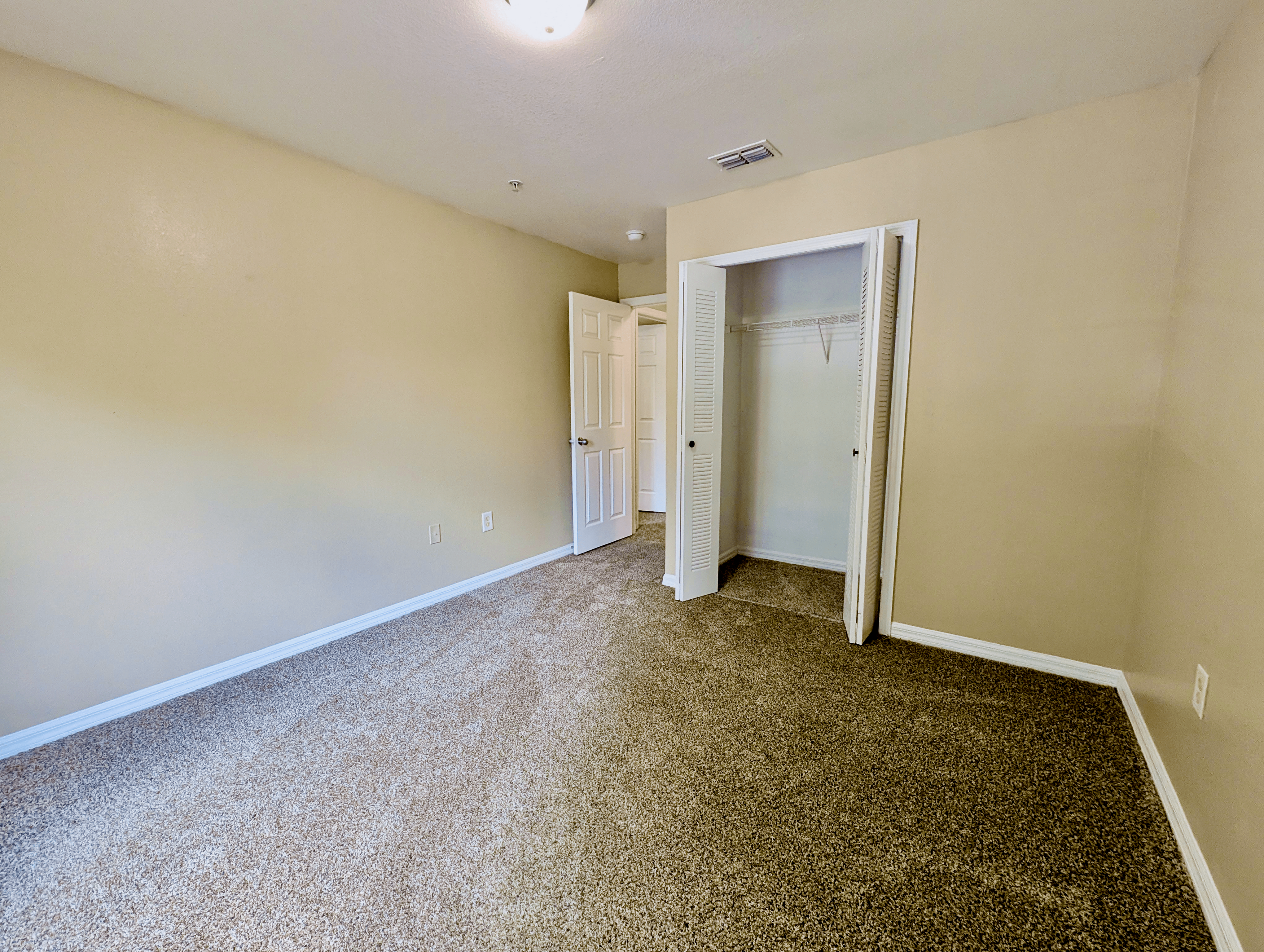 Bright and airy bedroom with plush carpet and open closet, perfect for a cozy and functional living space.