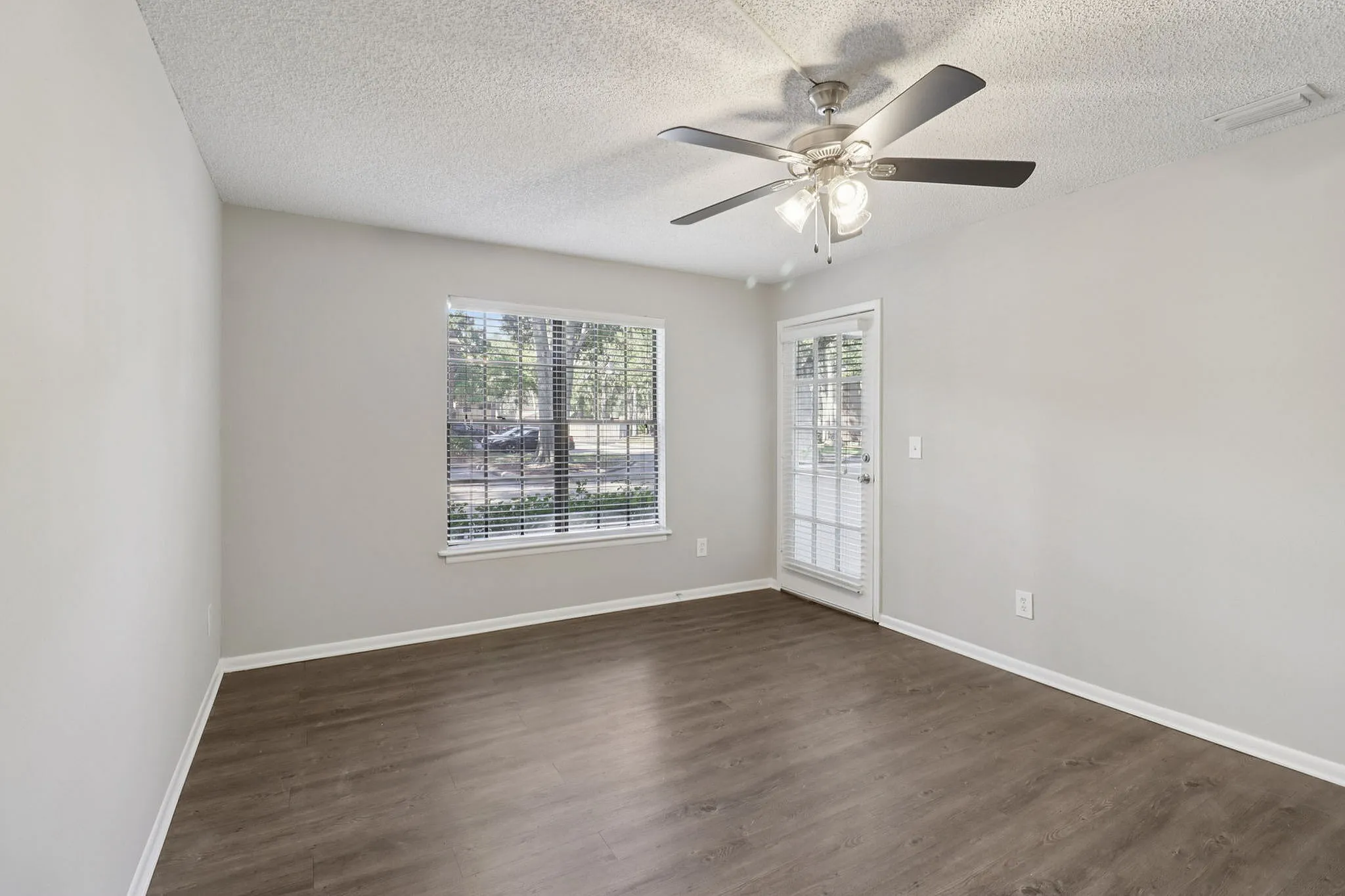 Bright room with elegant wood flooring, large window, and modern ceiling fan, perfect for comfortable living.