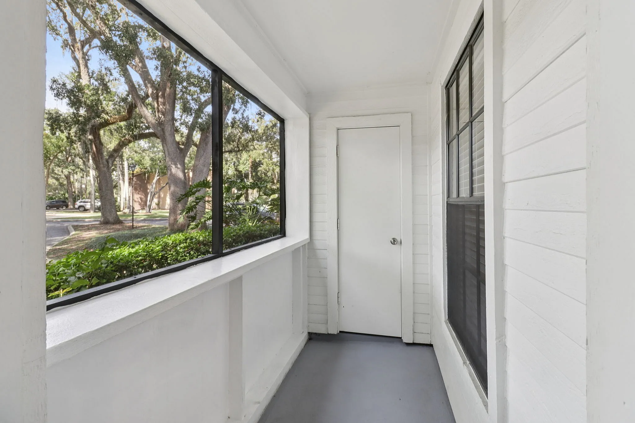 Inviting enclosed porch with large windows showcasing a serene view of lush trees, perfect for relaxing and enjoying nature.