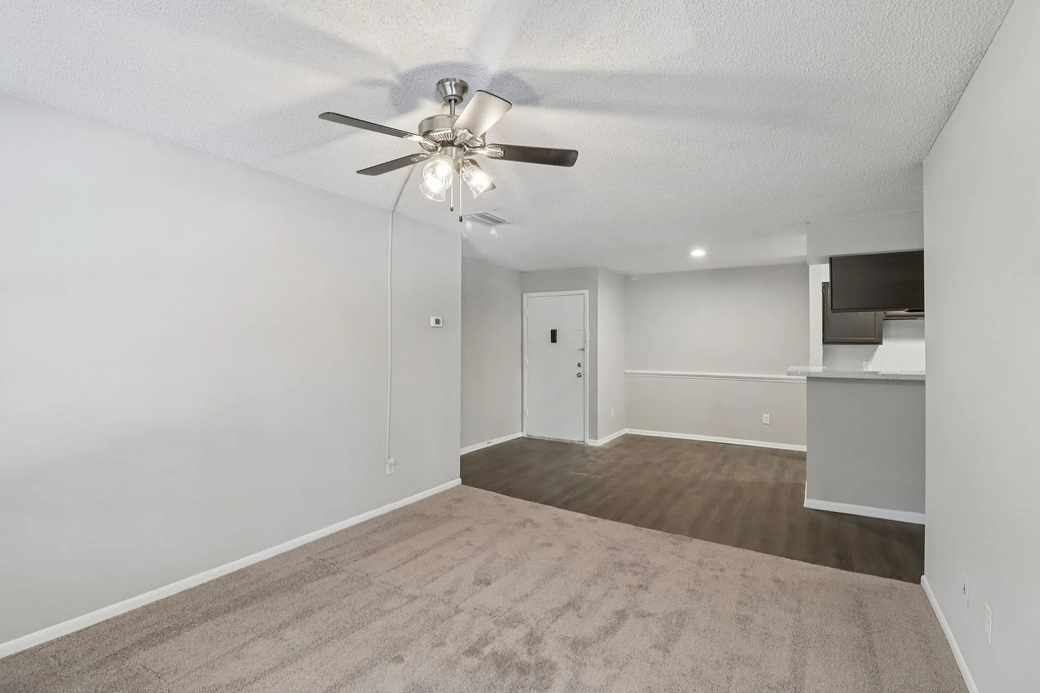 Inviting living space featuring plush carpet, sleek hardwood floor transition, and modern ceiling fan in an open layout apartment.