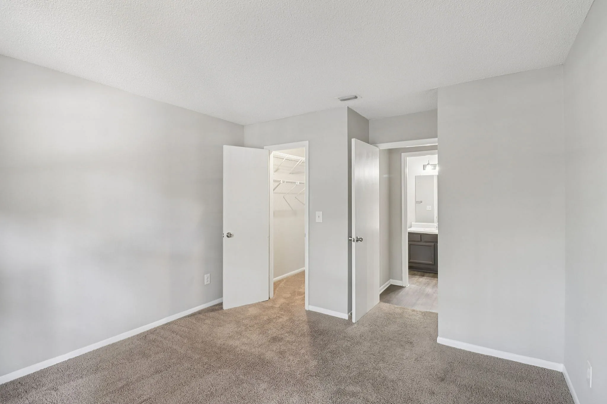 Bright and spacious bedroom with plush carpeting, featuring a walk-in closet and an adjoining bathroom with modern fixtures.