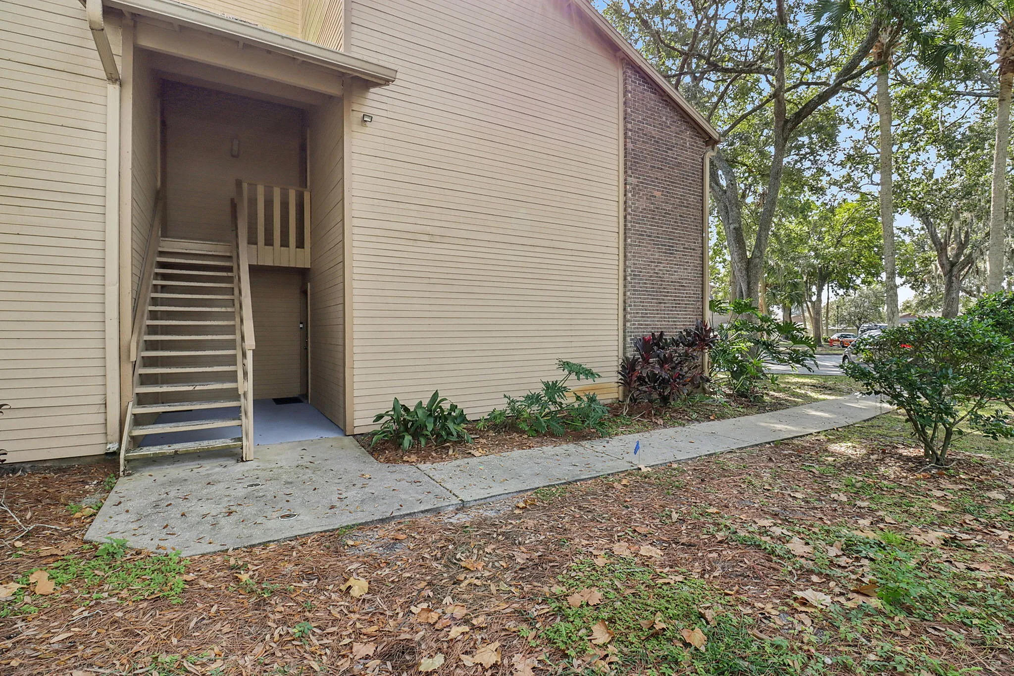 Charming apartment entrance with rustic wood siding and inviting staircase, surrounded by lush greenery and mature trees.