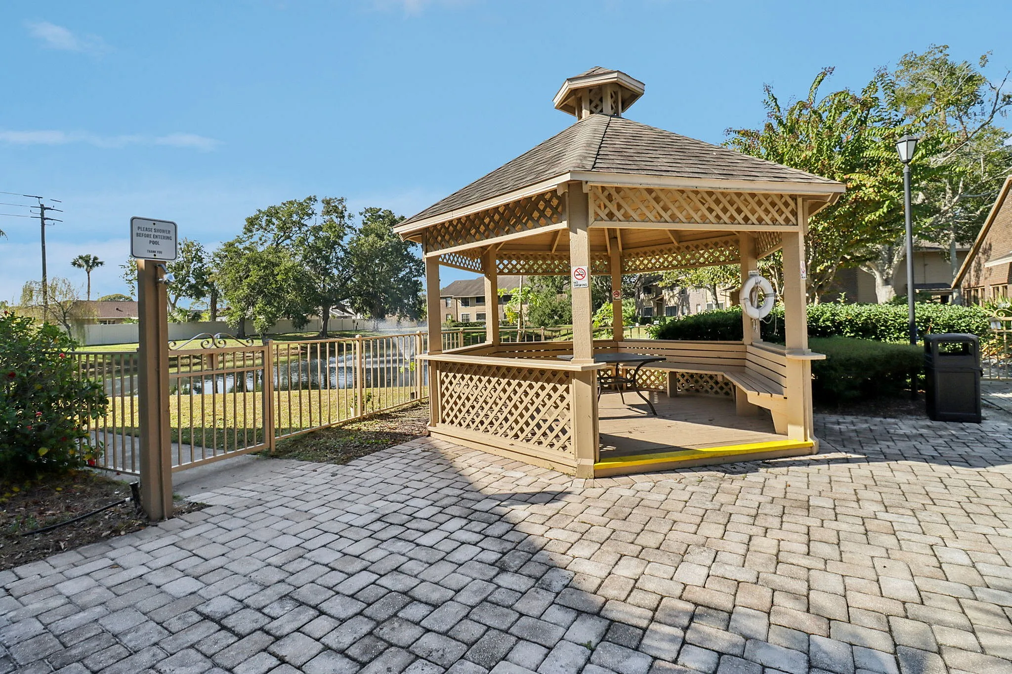 Charming outdoor gazebo with tiled walkway, surrounded by lush greenery and scenic pond views.