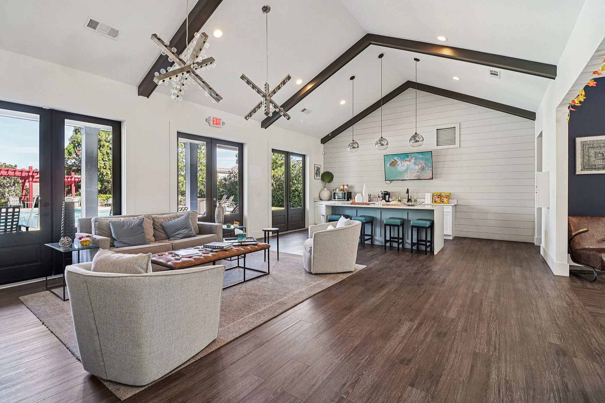 Elegant open-concept clubhouse with vaulted ceilings, featuring modern lighting, cozy seating, and a chic kitchen with bar stools and stylish decor.