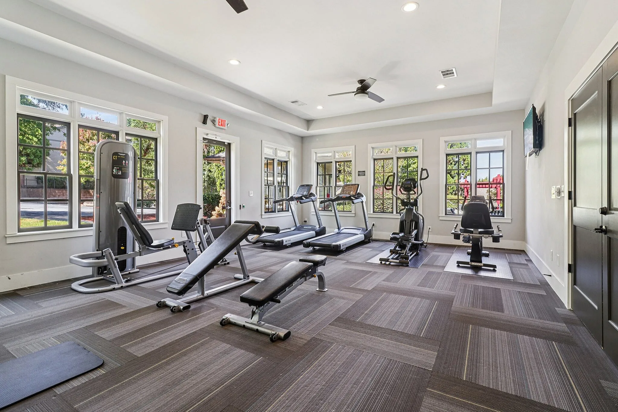 Bright, modern gym with large windows, featuring state-of-the-art equipment including treadmills, elliptical machines, and benches.