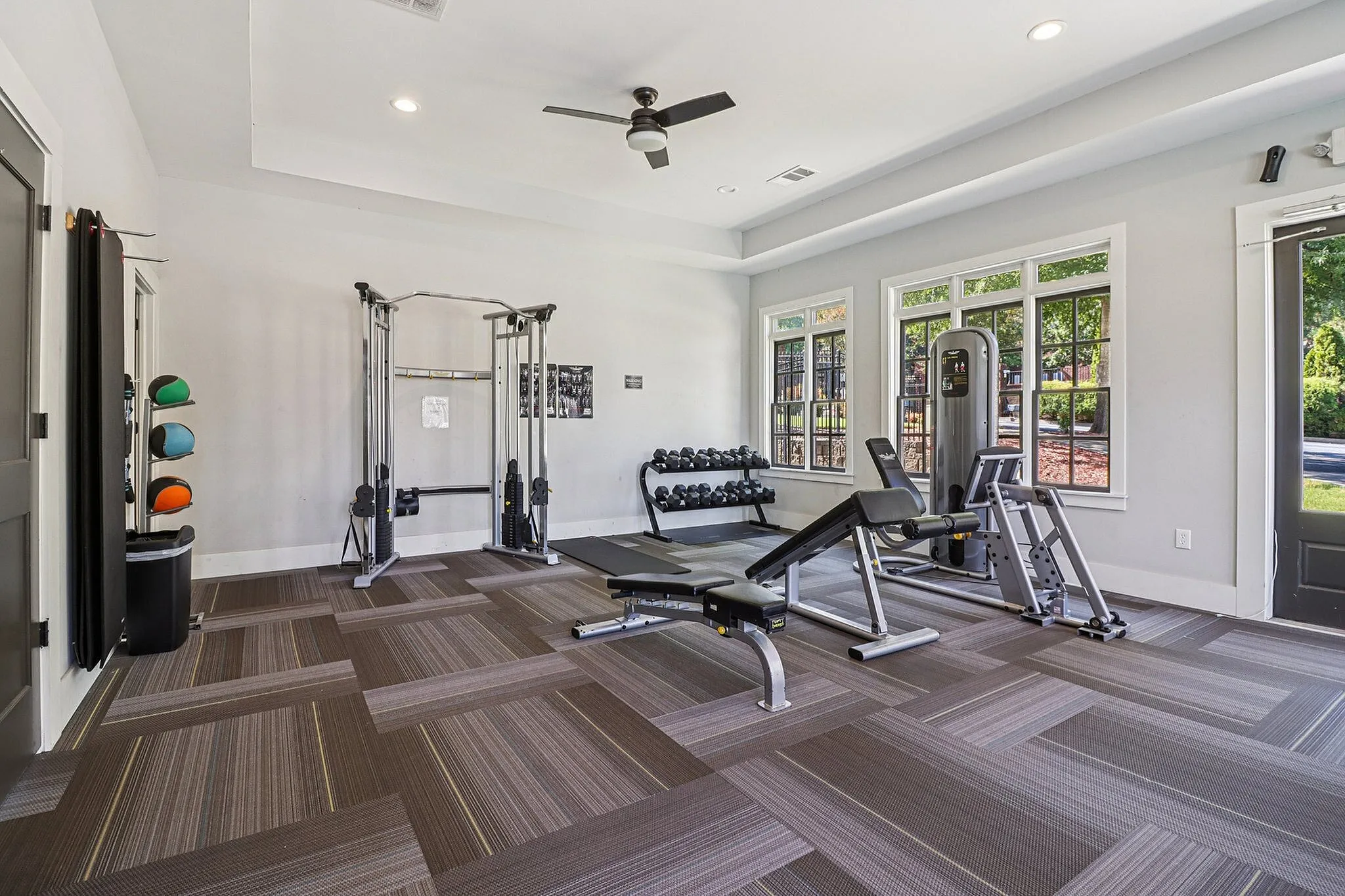 Bright and inviting gym room featuring modern workout equipment, free weights, and large windows letting in natural light.
