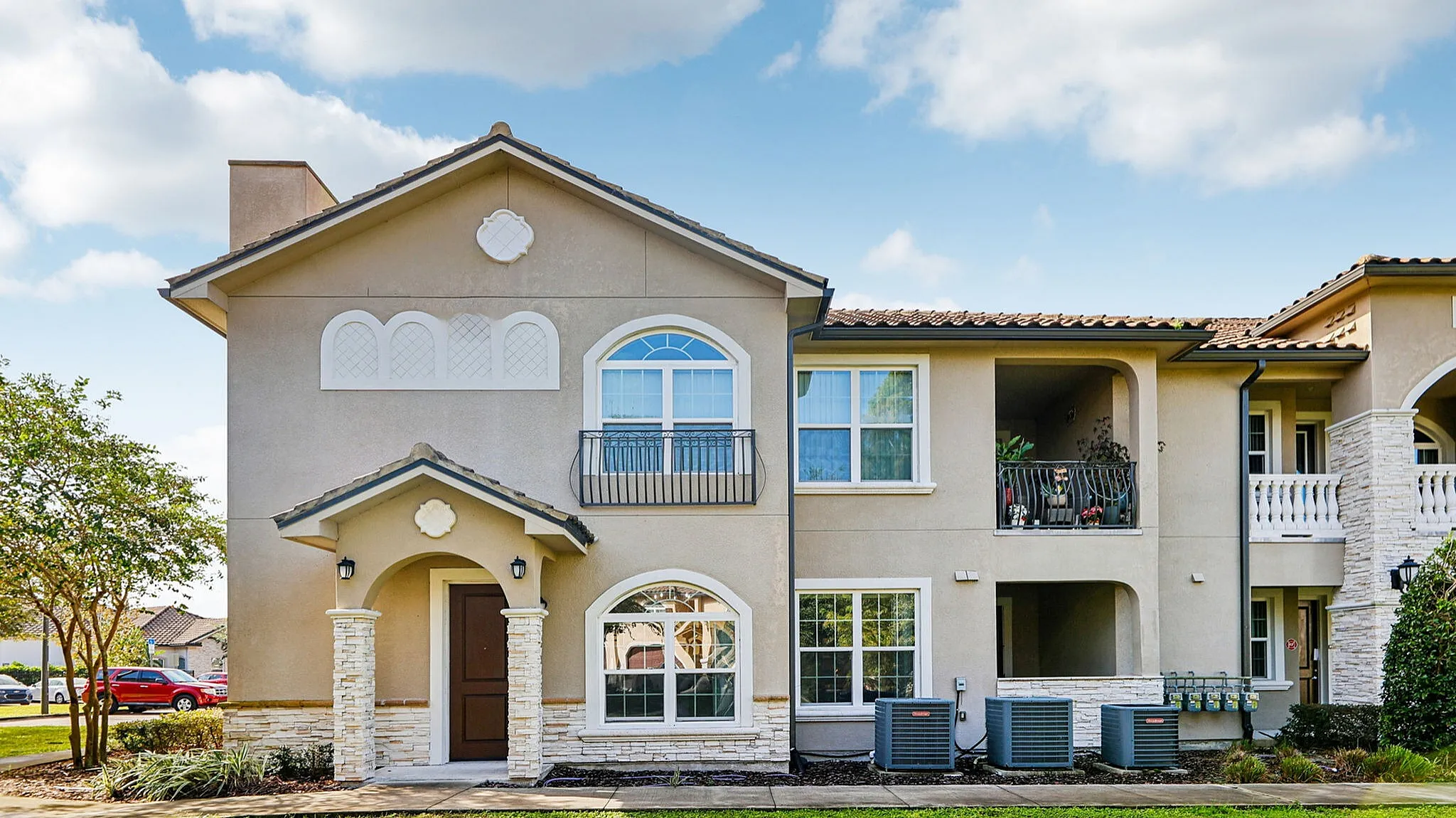 Charming two-story apartment building with elegant balconies and stone accents, set against a bright blue sky.