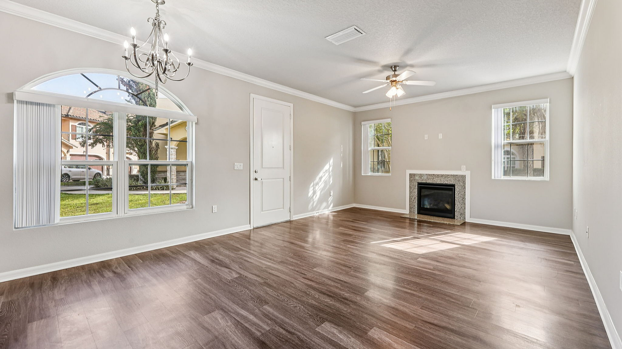 Inviting living room with elegant chandelier, large sunlit windows, and cozy fireplace, featuring sleek hardwood flooring.