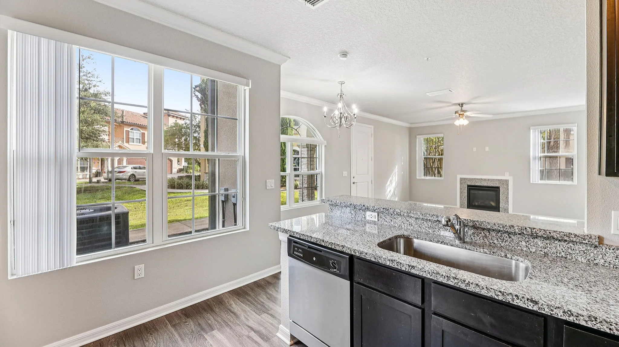 Bright and inviting living area with stylish granite countertops, modern chandelier, and large windows overlooking a serene neighborhood view.