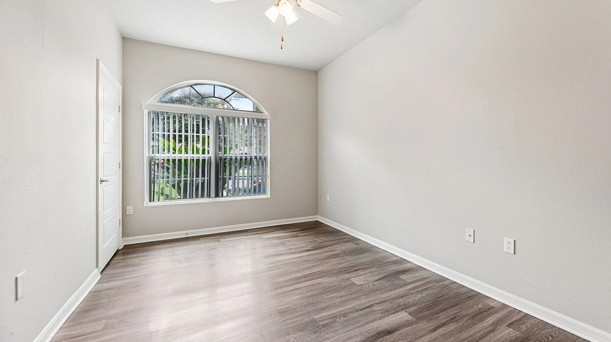 Bright and inviting bedroom featuring elegant hardwood floors, large arched window, and soothing neutral walls.