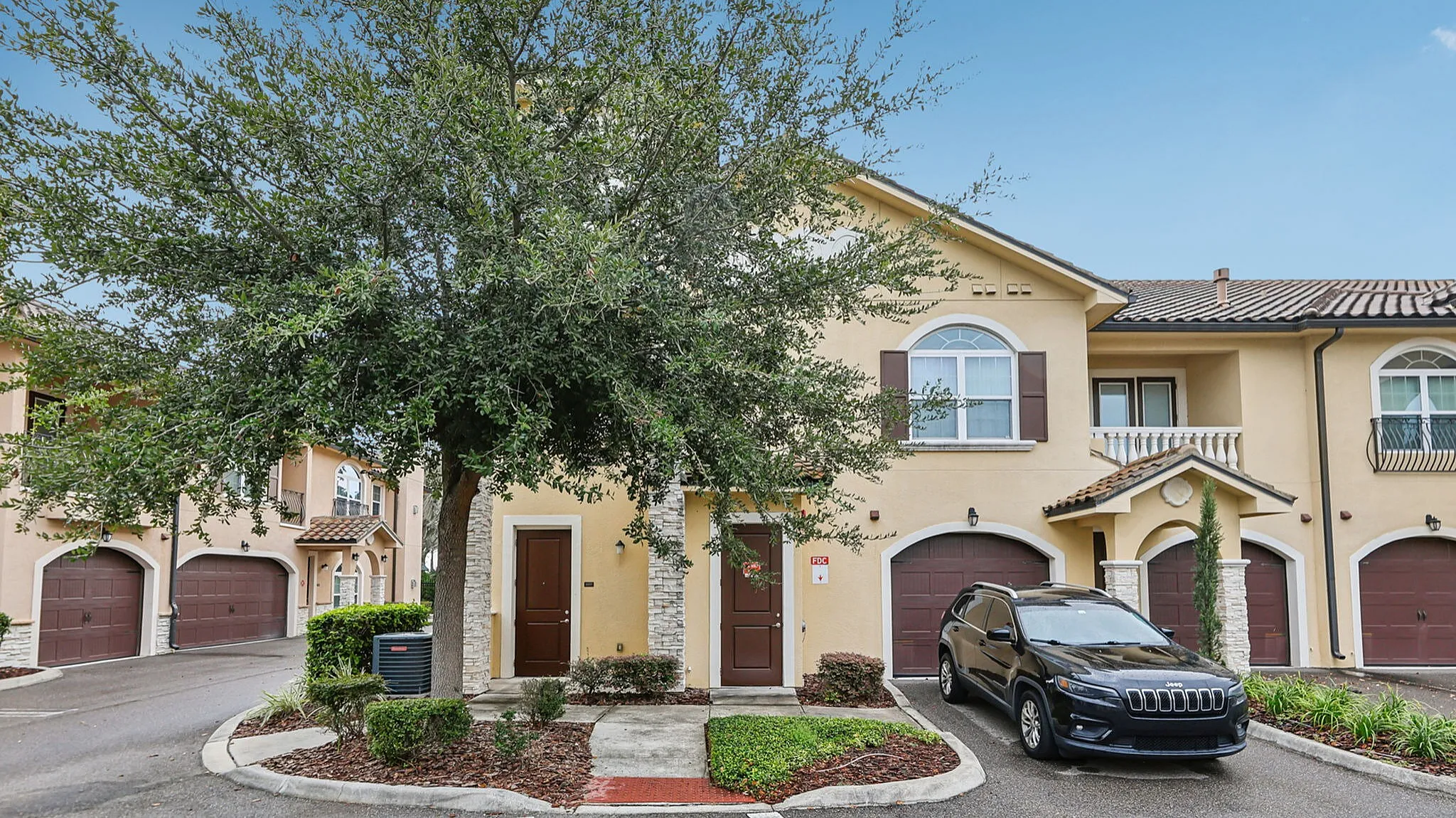 Charming townhouse with classic architecture, lush greenery, and attached garage in a serene neighborhood setting.