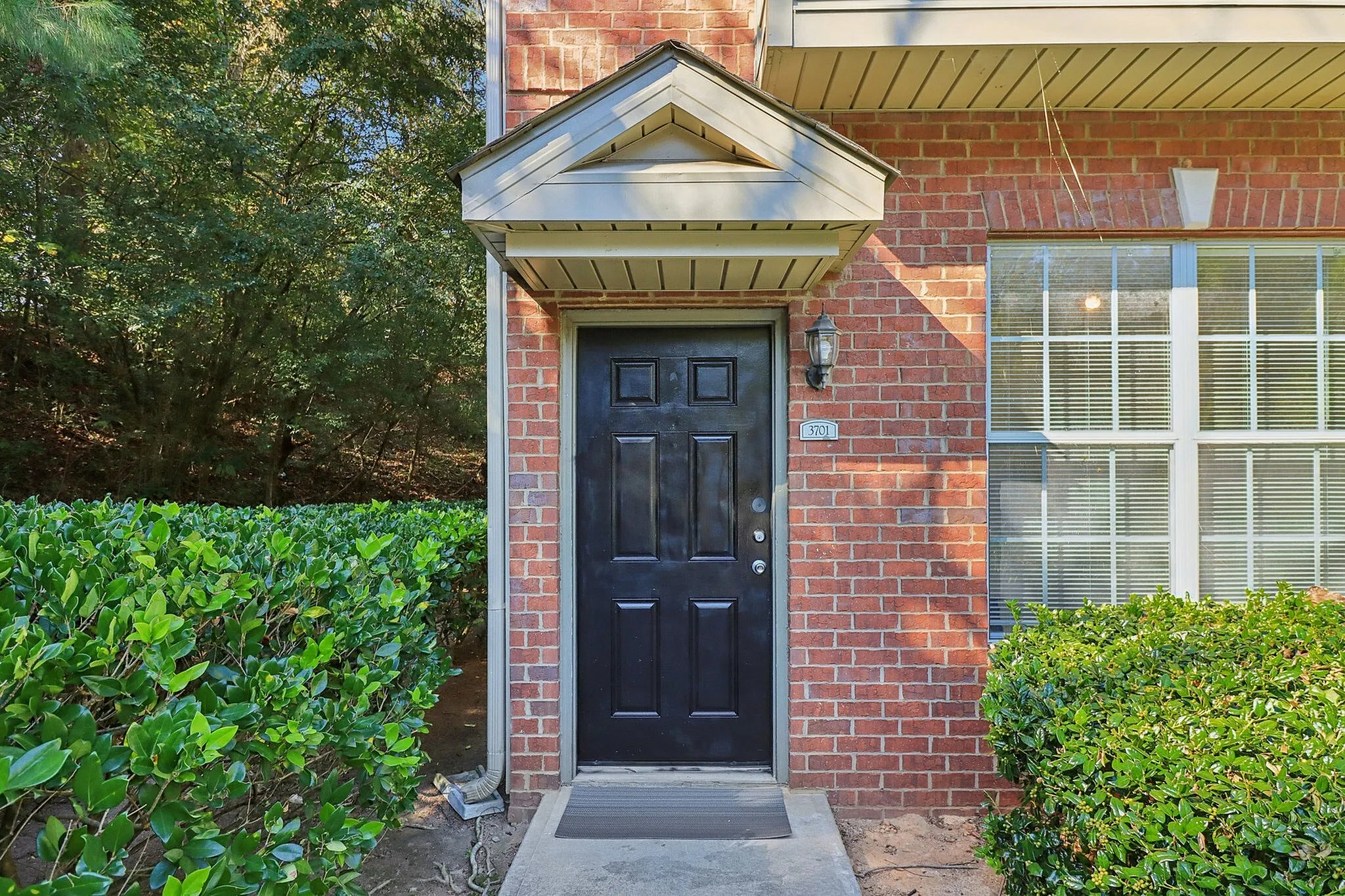 Inviting brick exterior with a stylish black door, framed by lush greenery for a warm welcome.