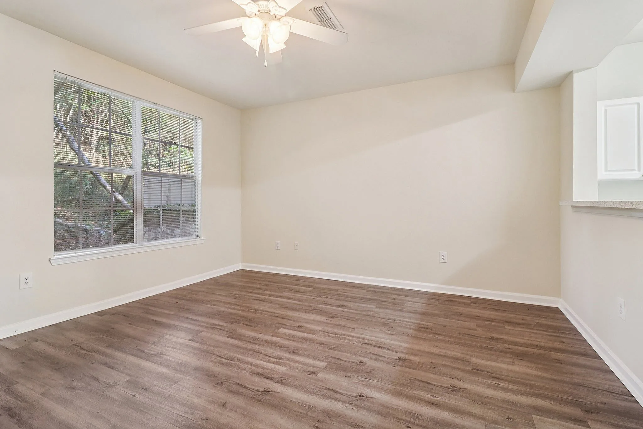 Bright living area with modern wood flooring, large window with garden view, and overhead ceiling fan.