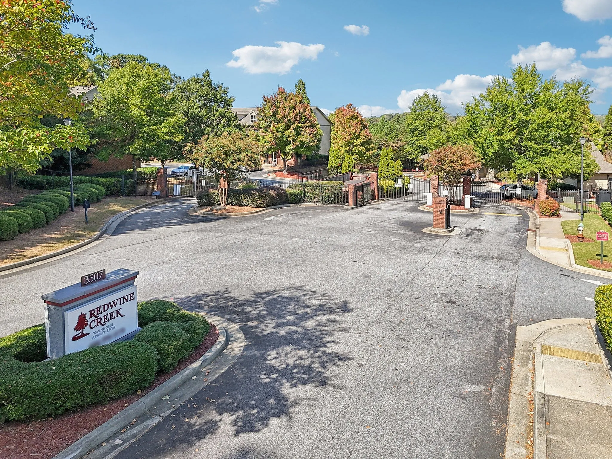 Inviting entrance to Redwine Creek Apartments, showcasing a gated community with lush greenery and a serene atmosphere.