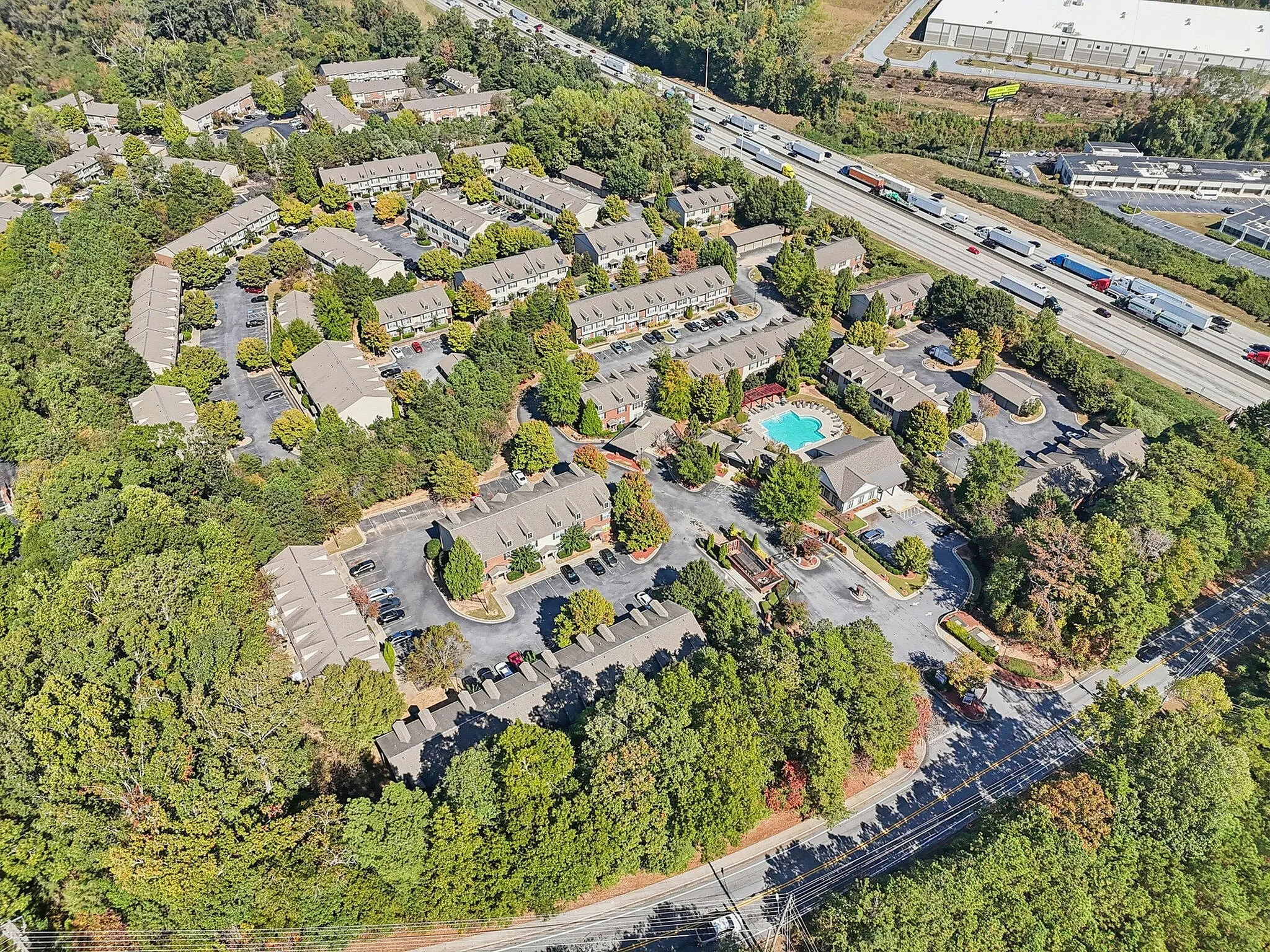 Aerial view of a vibrant apartment complex featuring lush greenery, spacious parking areas, and a refreshing central swimming pool, offering a serene residential oasis.
