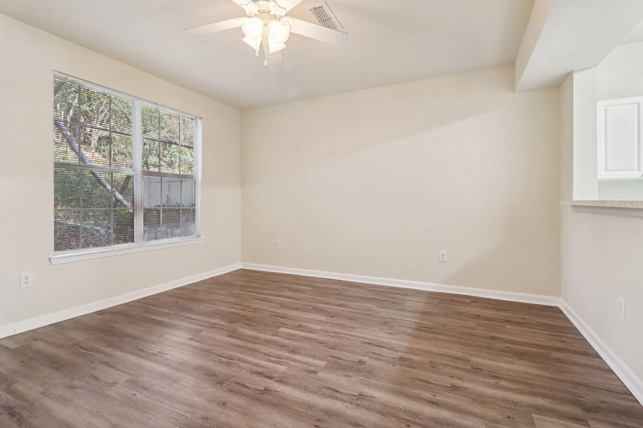 Bright and inviting living space with large window, elegant ceiling fan, and stylish wood flooring.