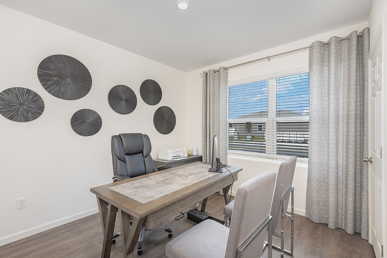 Bright and inviting home office with modern decor, featuring a sleek wooden desk and comfortable seating, complemented by stylish wall accents and a large window with a scenic view.