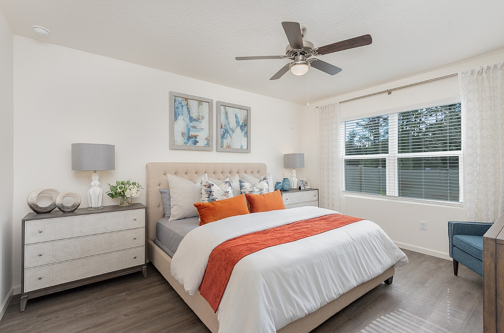 Bright and inviting bedroom with modern decor, featuring a plush bed with vibrant pillows, elegant bedside lamps, and large windows letting in natural light.