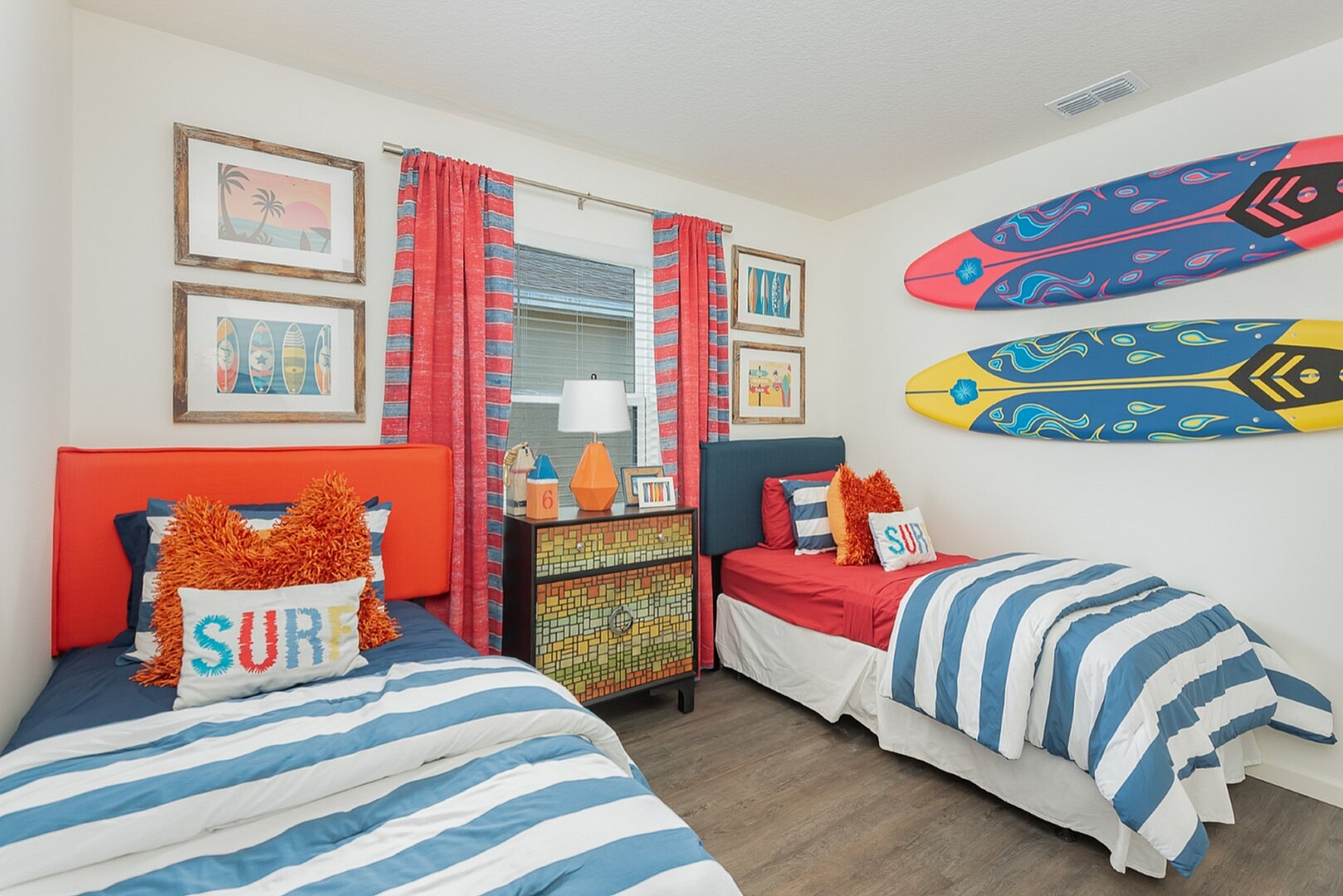 Vibrant nautical-themed bedroom with two cozy twin beds adorned in blue and white stripes, surfboard wall decor, and colorful ocean-inspired accents.