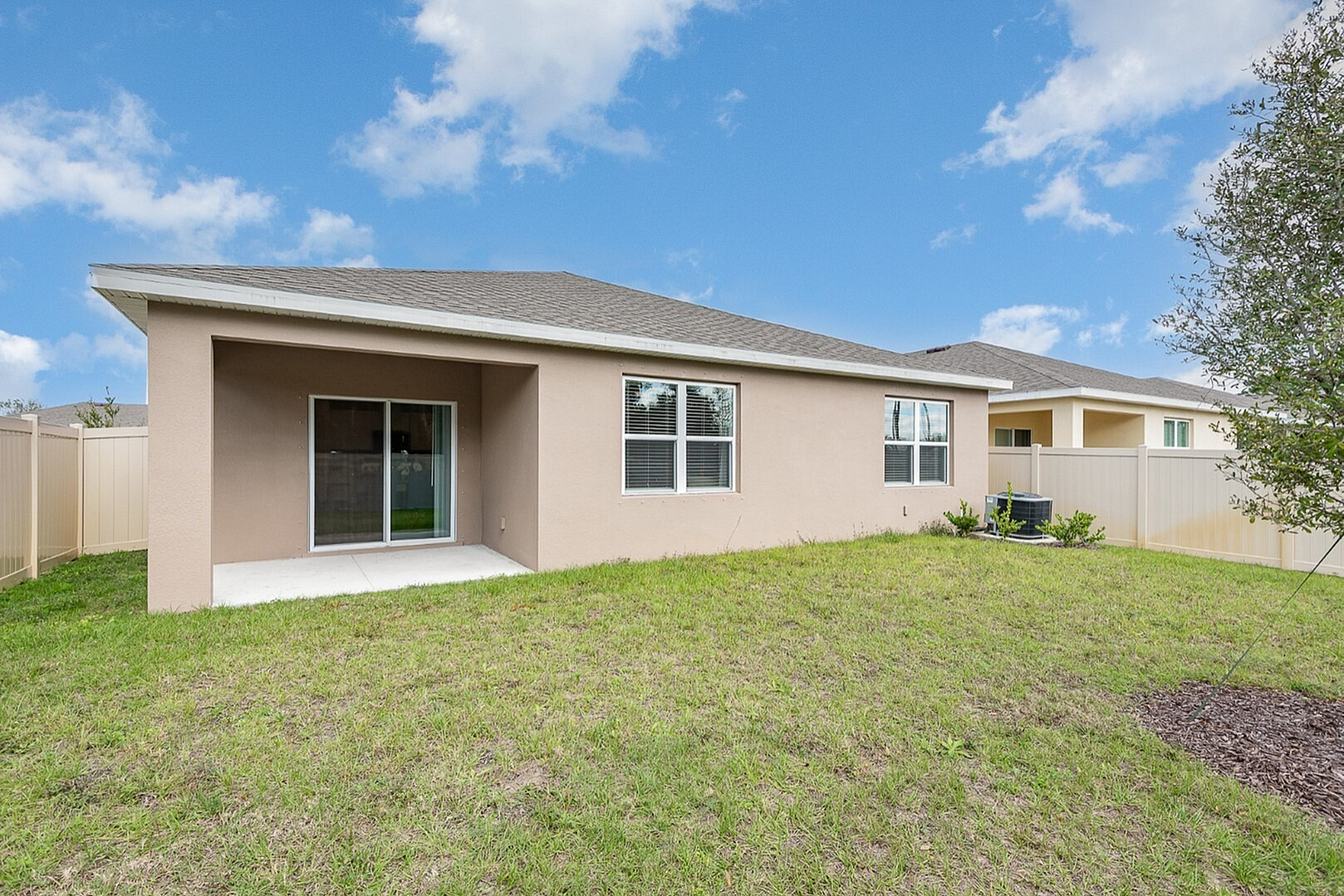Charming backyard view of a modern single-story home with a spacious lawn, a covered patio, and a perfect mix of privacy and comfort.