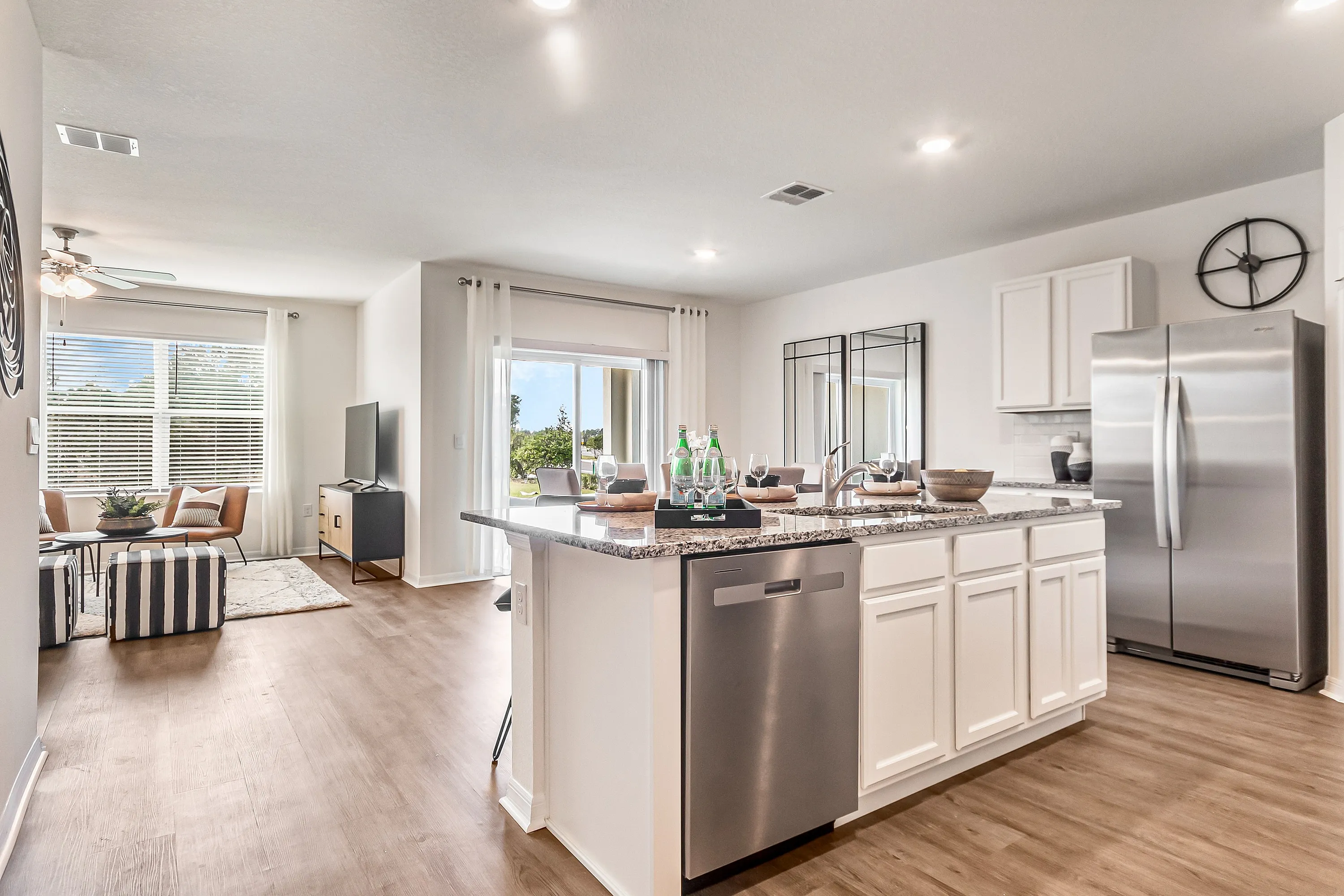 Modern open-concept kitchen with sleek granite countertops and stainless steel appliances, leading to a bright, inviting living area with large windows and chic decor.