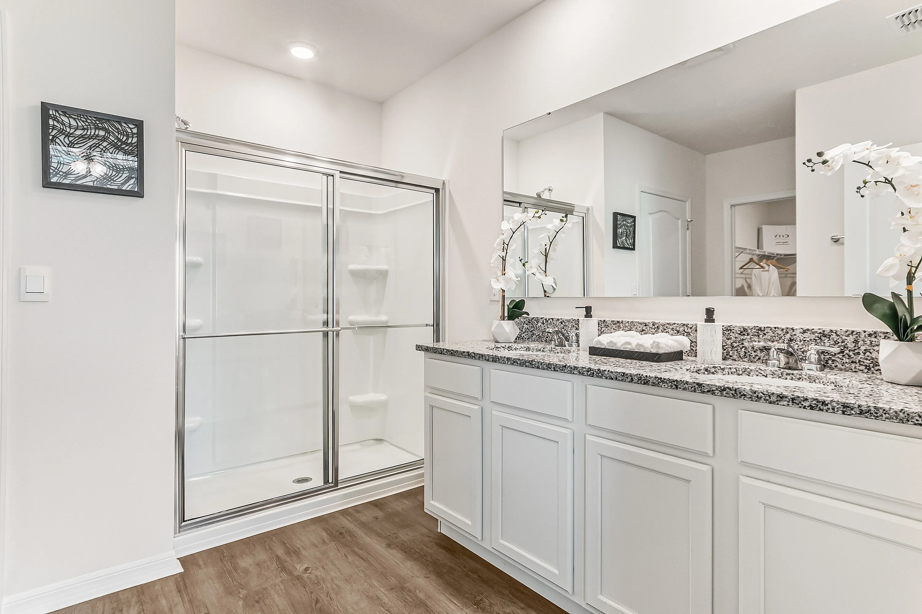 Elegant bathroom with a granite double vanity, modern fixtures, and spacious glass-enclosed shower.