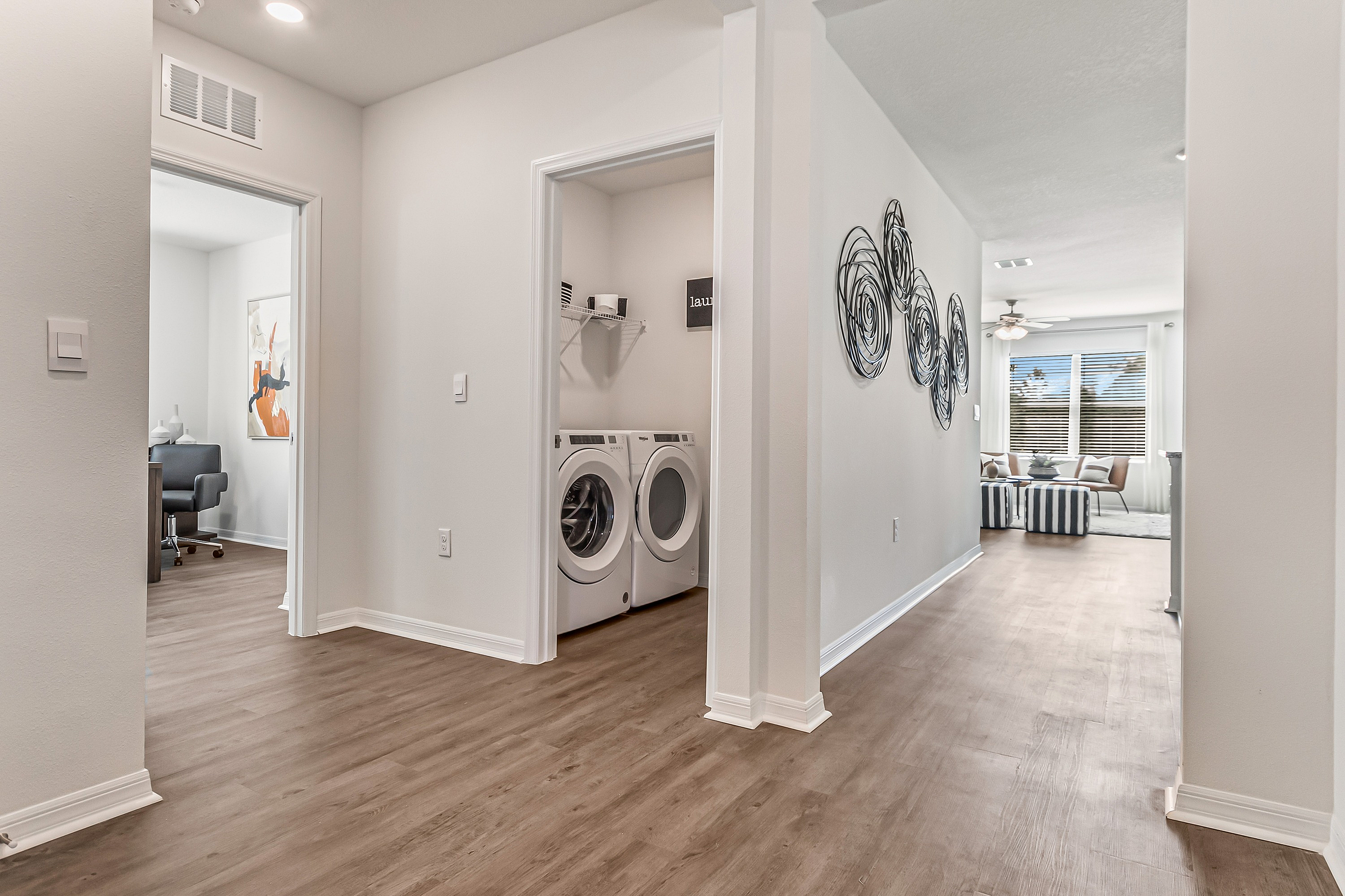 Elegant apartment hallway showcasing chic interior design, featuring modern laundry amenities and a glimpse of a stylish living area with large windows.